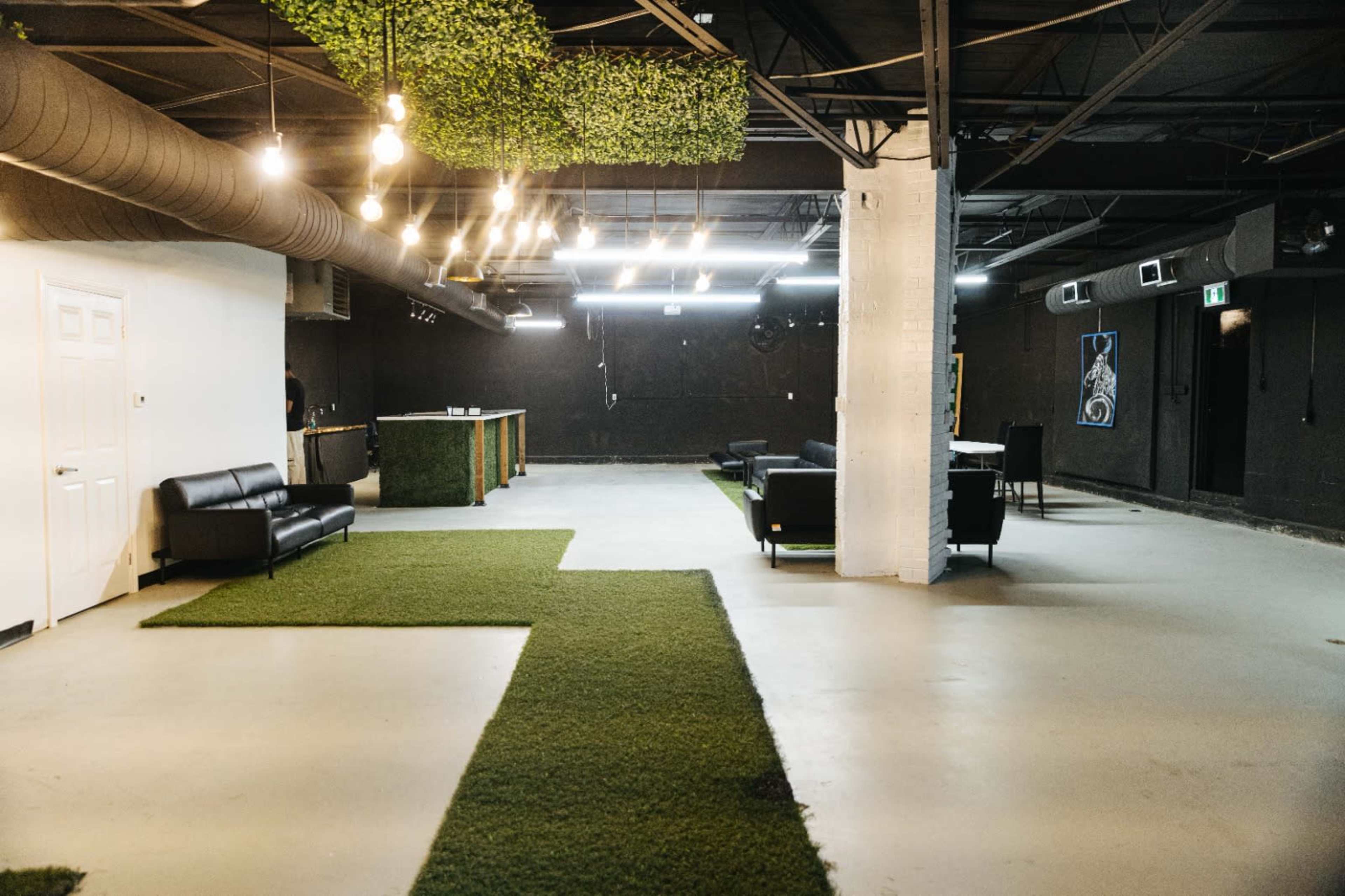 A minimalist interior space with artificial grass flooring, a black sofa, and bright overhead lights.