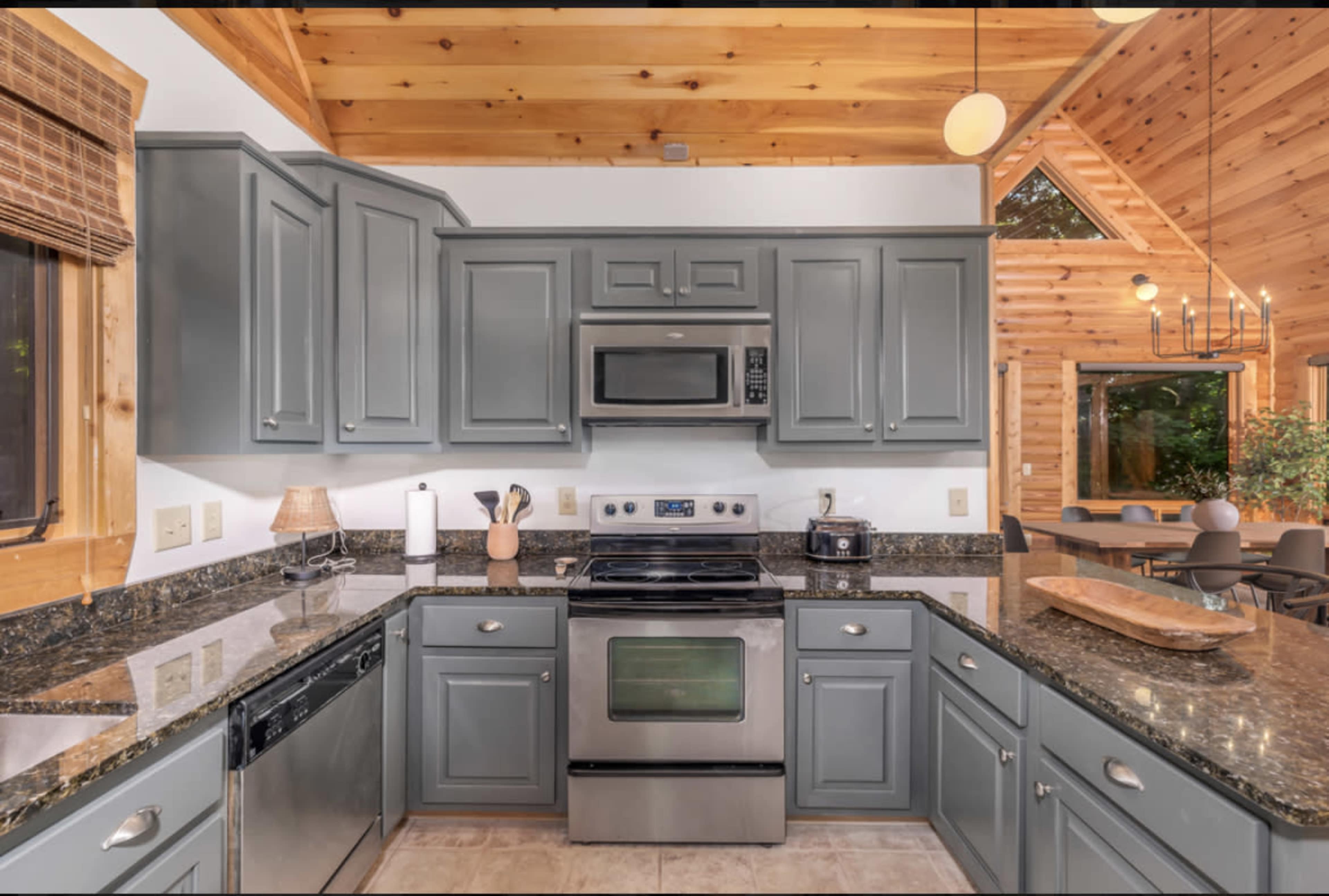 The image shows a modern kitchen with gray cabinets, a stainless steel microwave, and a dark granite countertop, adjacent to a dining area with wooden accents.