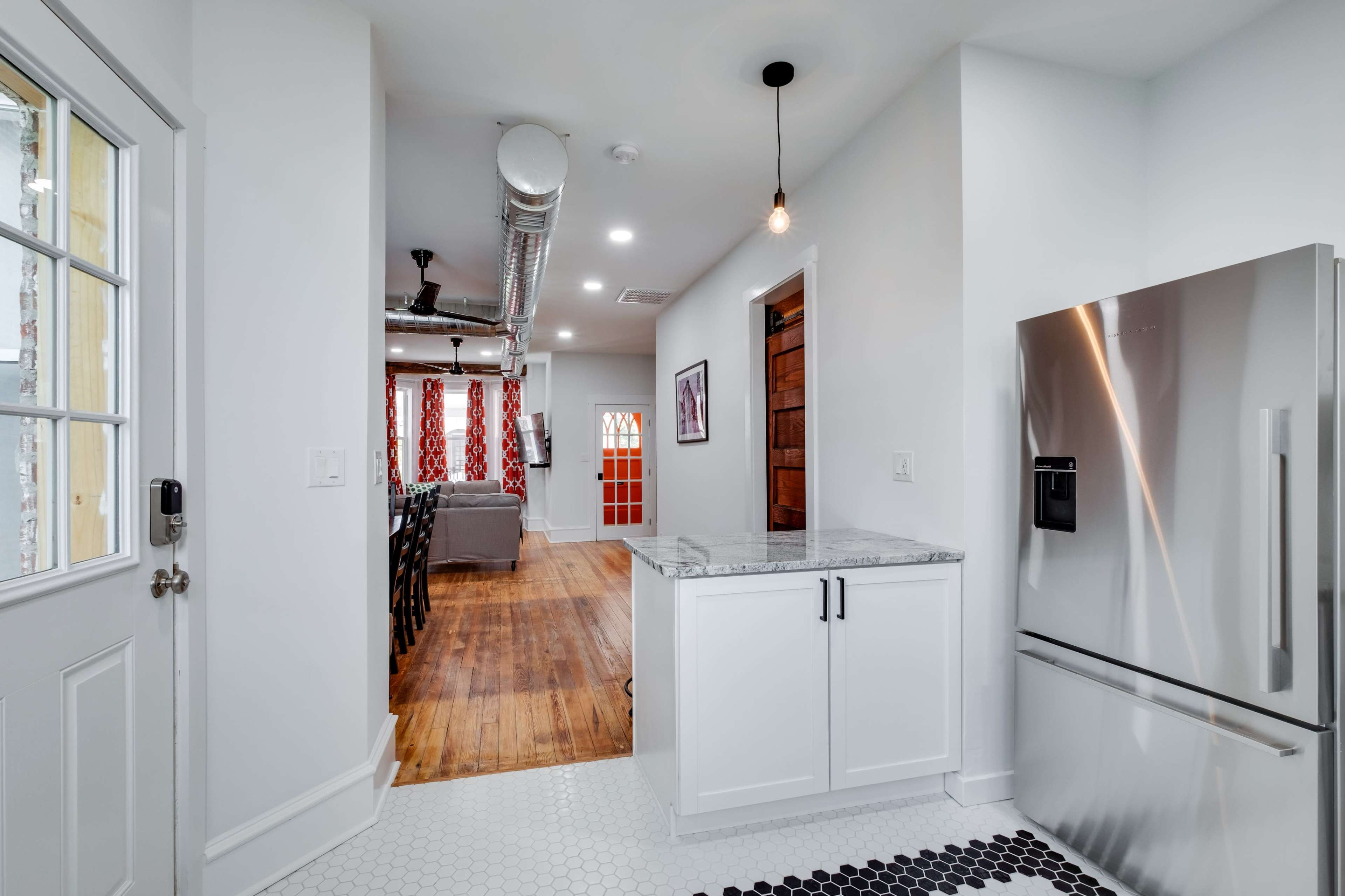 A modern kitchen features a stainless steel refrigerator, white cabinets, and a view into a living area with a cozy seating arrangement.