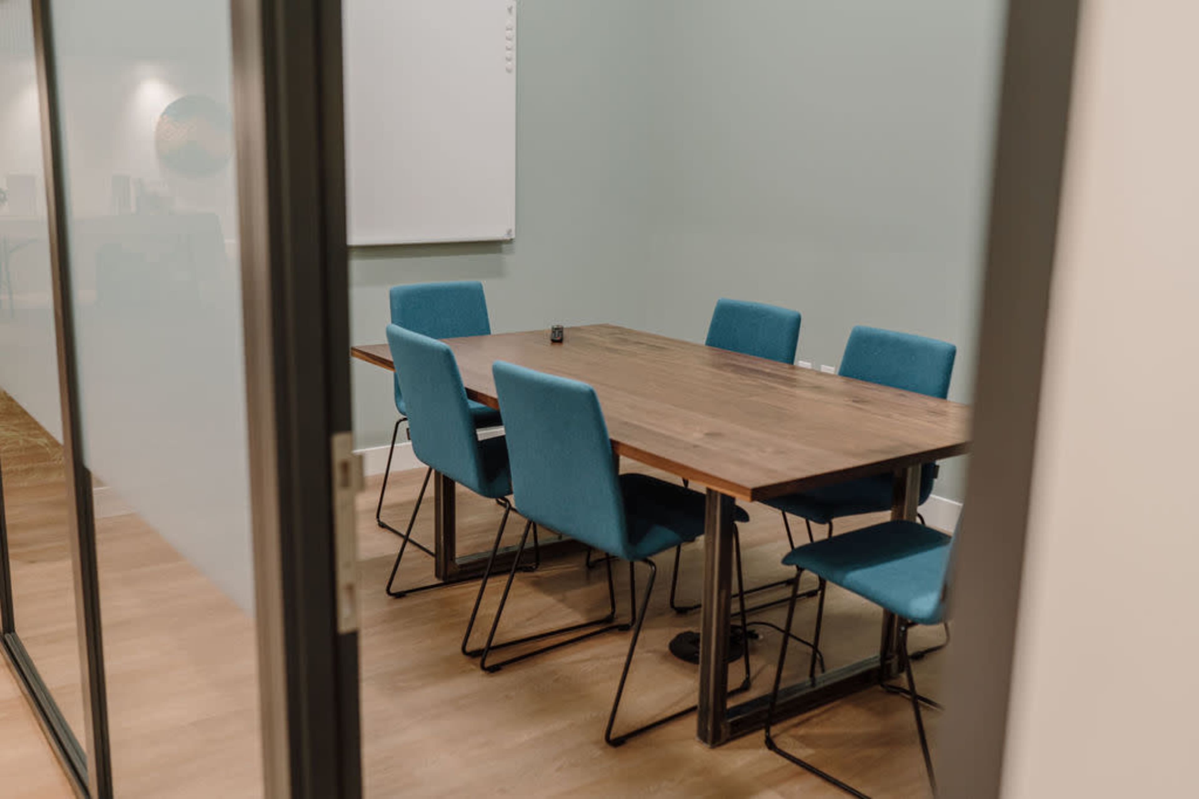 A conference room features a large wooden table surrounded by six blue chairs.