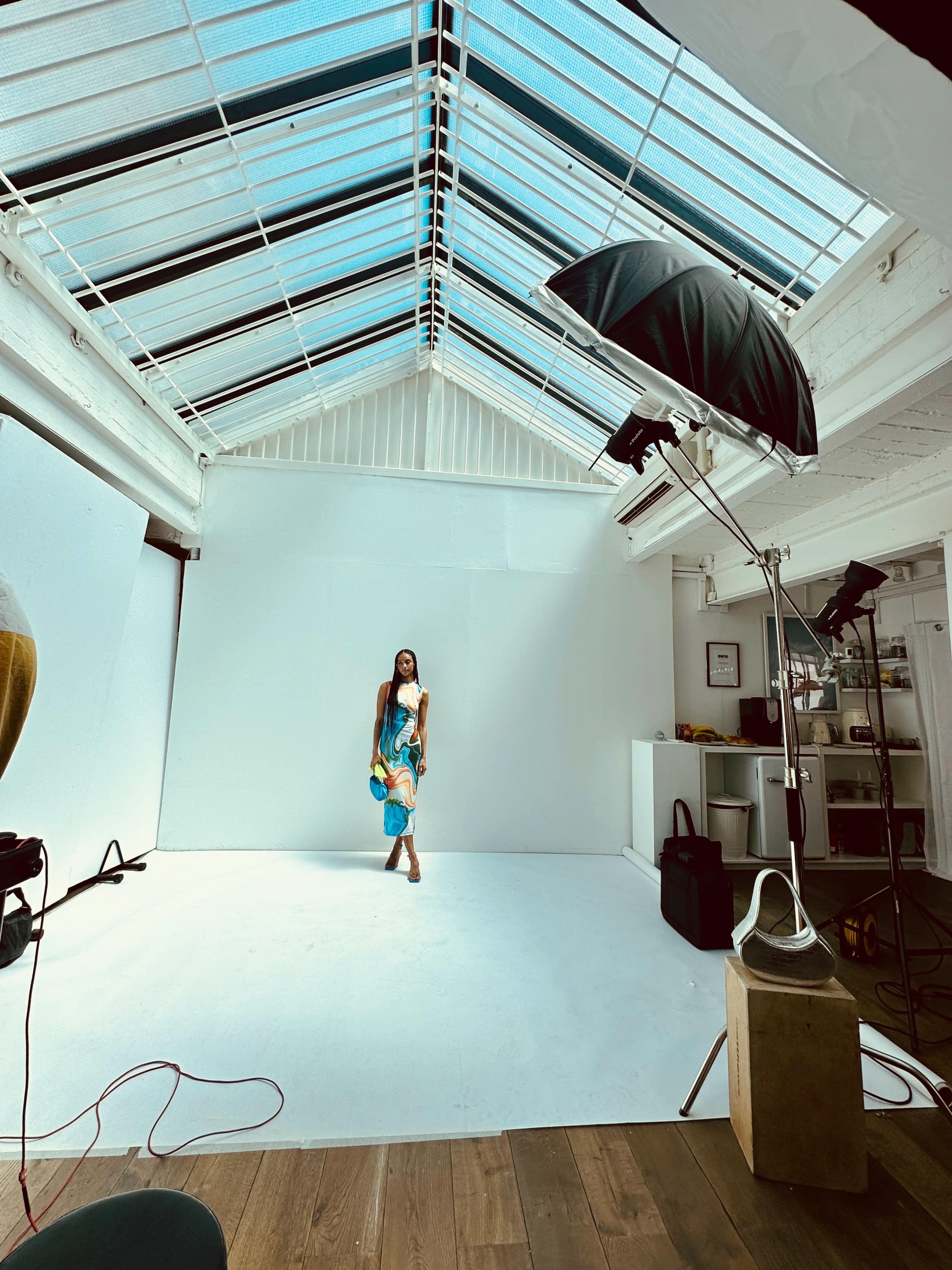 A model holds blue props while standing in a bright, empty photography studio with a slanted glass roof.