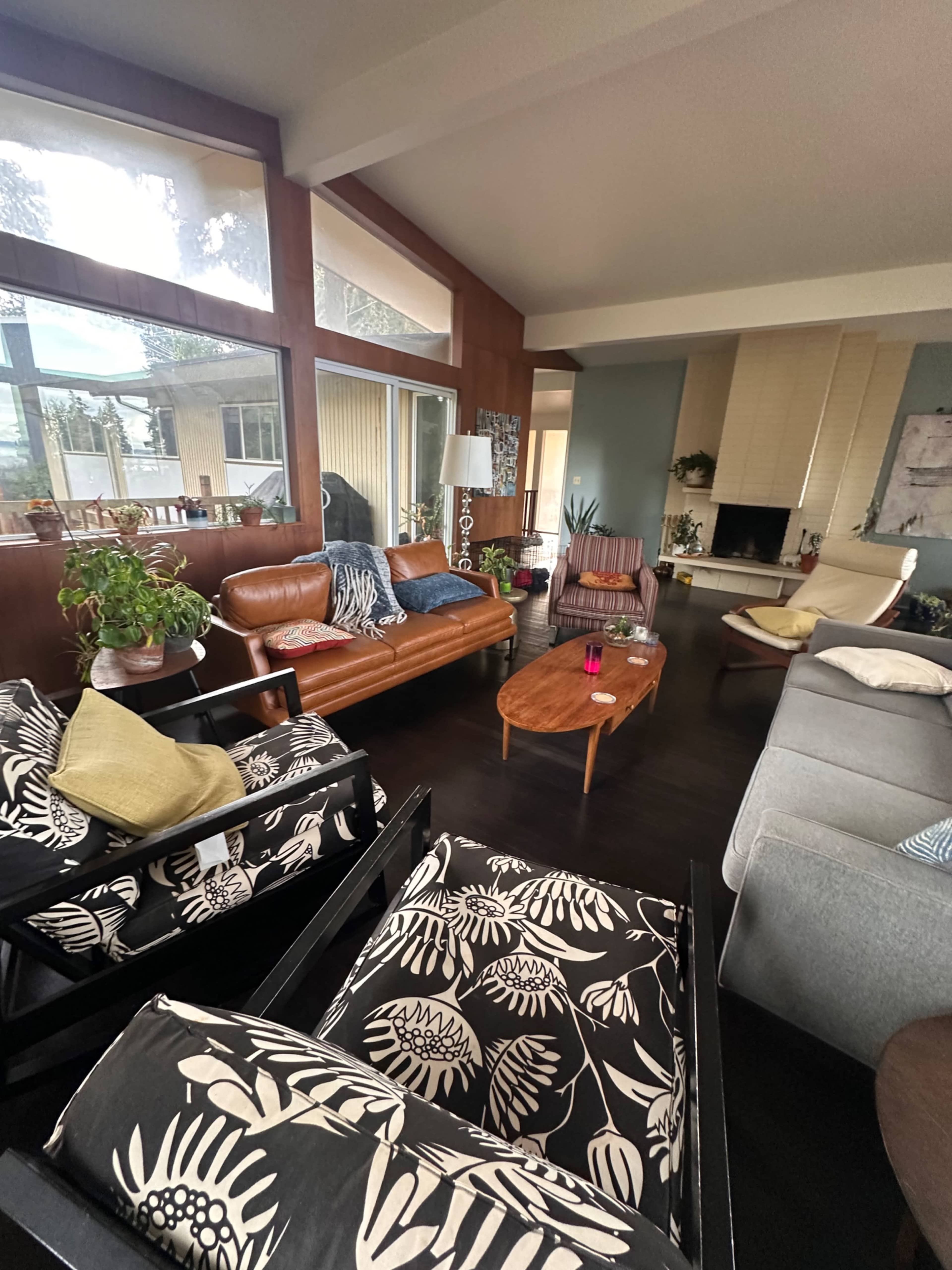 The image shows a modern living room with various seating options, including a leather sofa and patterned chairs, along with a coffee table and large windows.
