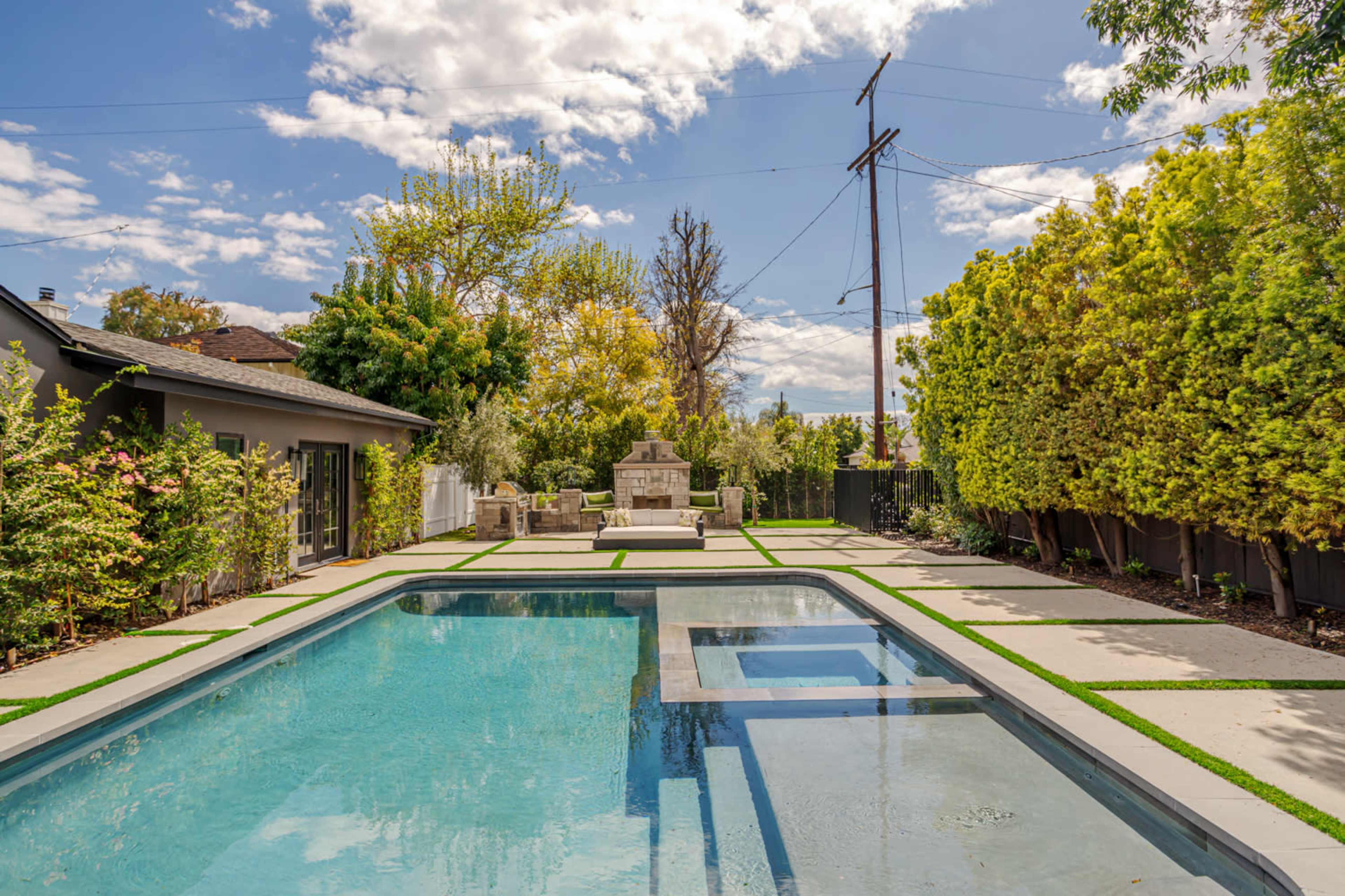 The image shows a backyard with a rectangular swimming pool, a spa area, and landscaped greenery on either side.