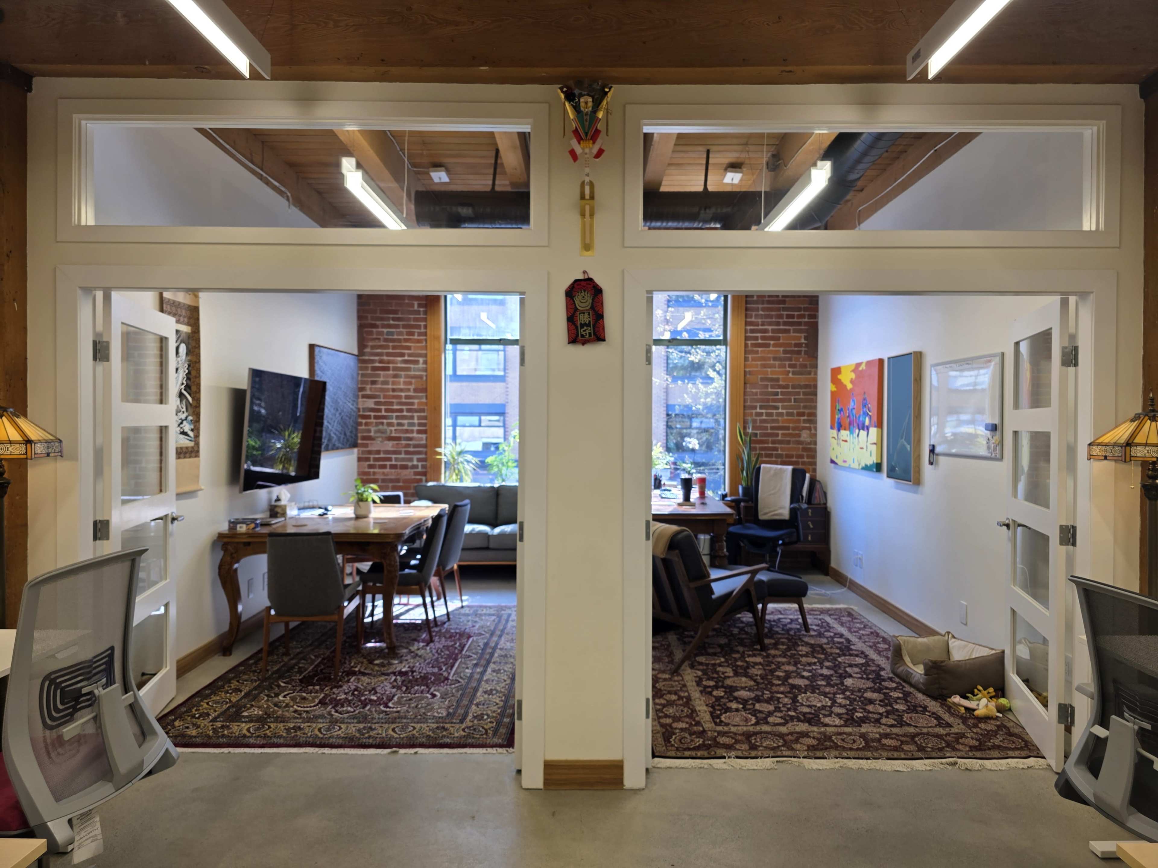 The image shows a split view of two office spaces with brick walls, a seating area, and artwork displayed on the walls.