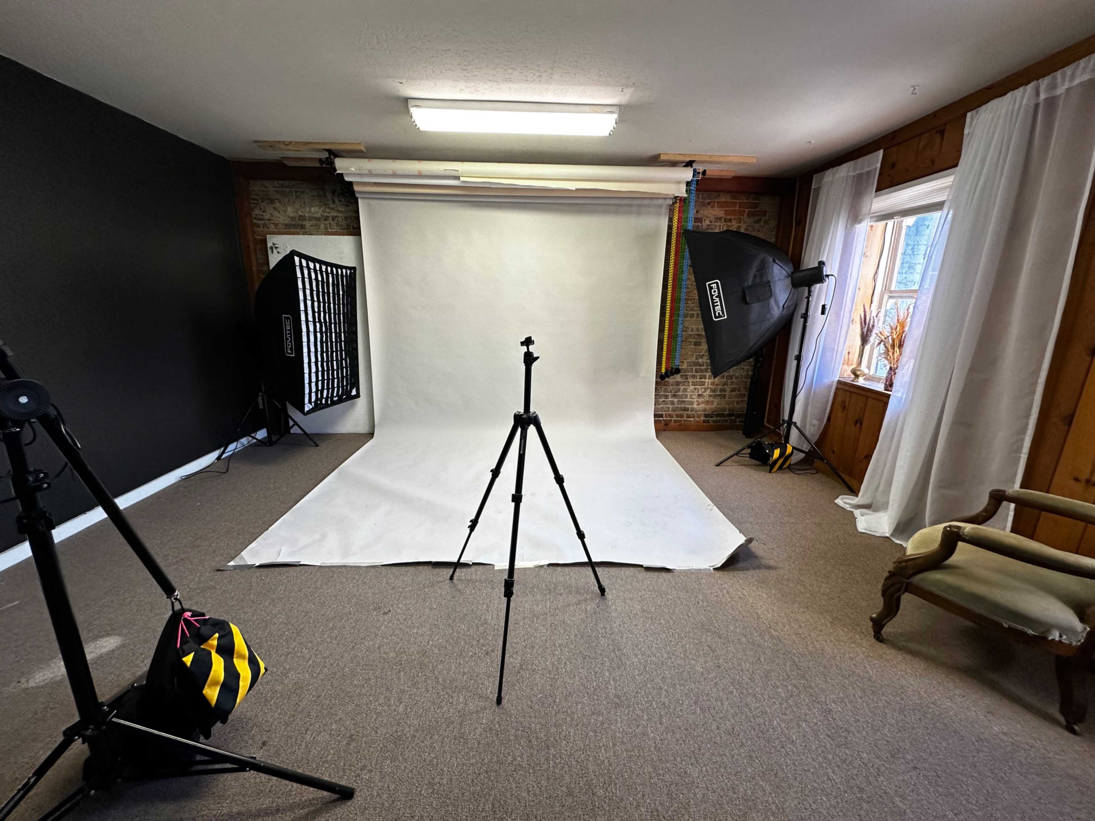 A photography studio setup with a white backdrop, lighting equipment on both sides, and a tripod positioned in the center.