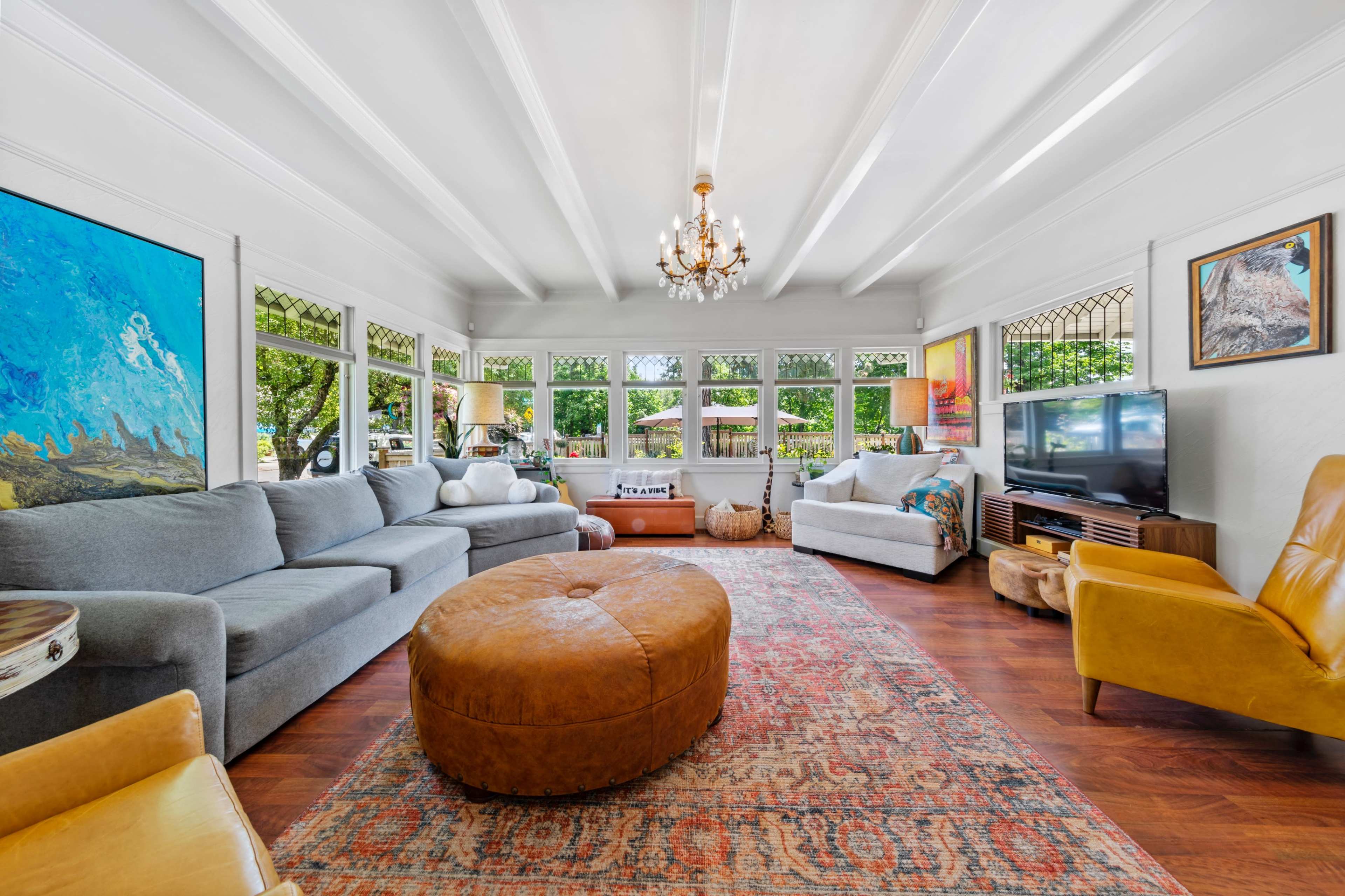 The living room features a large area rug, a round ottoman, a sectional sofa, and multiple windows allowing natural light.