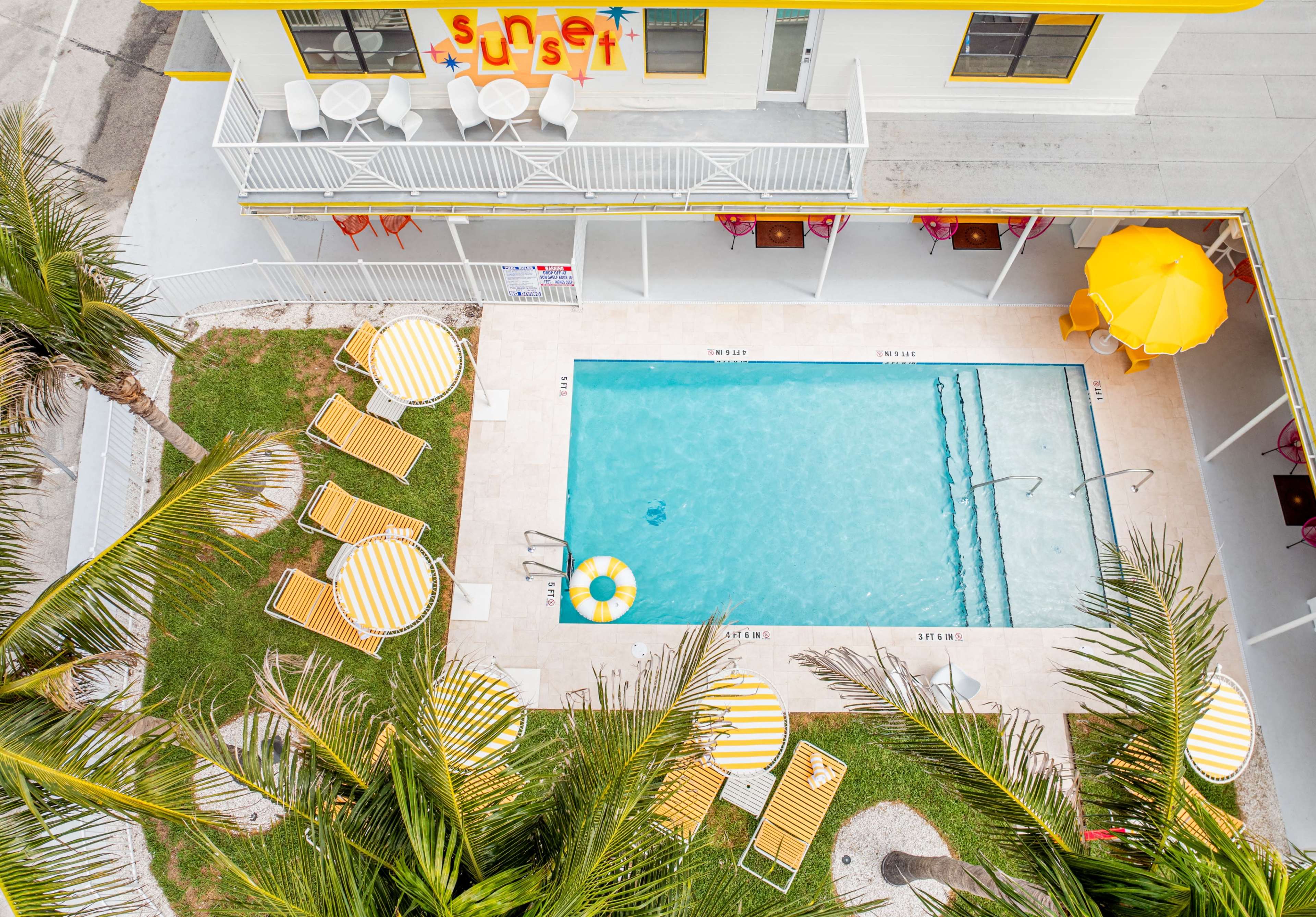 The image shows an overhead view of a swimming pool surrounded by lounge chairs and a yellow umbrella at a hotel with a sign that reads "sunset."