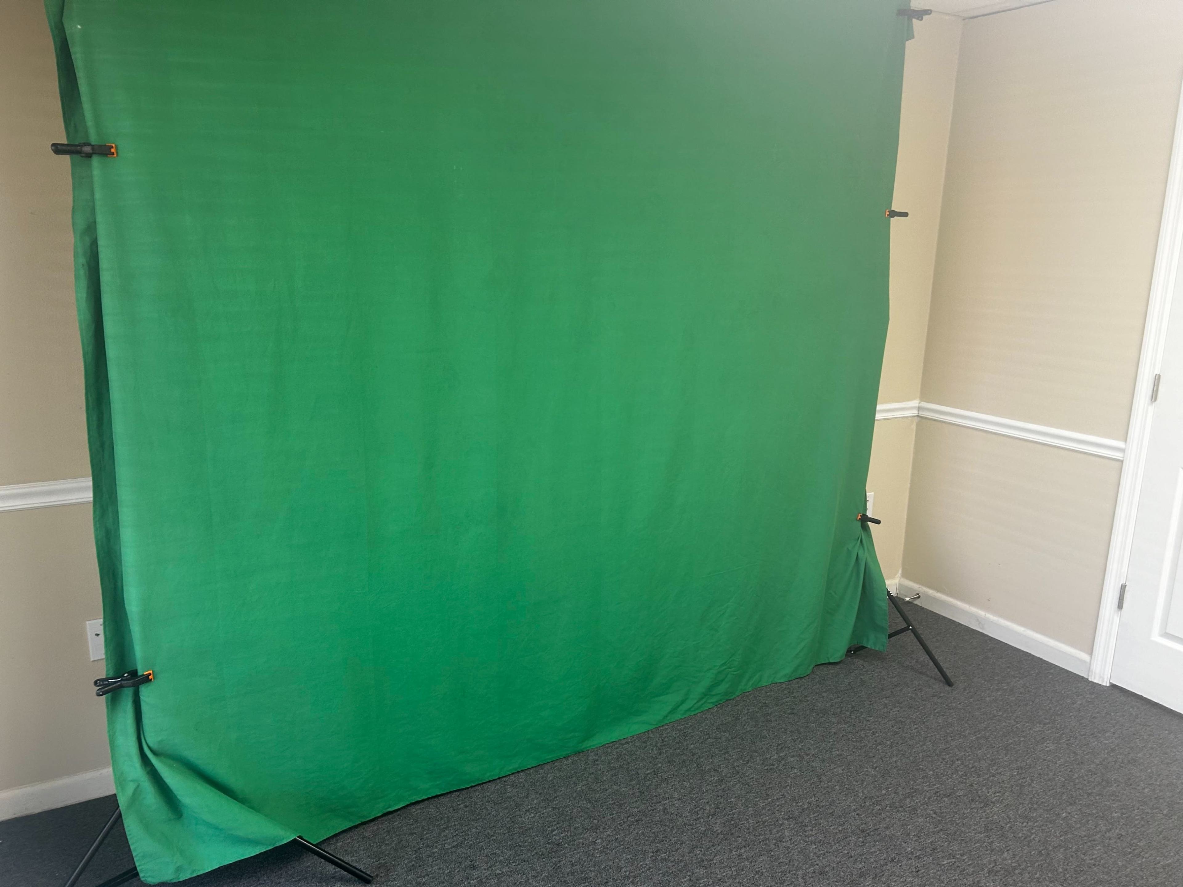 A green backdrop is set up in a room with beige walls and gray carpet.