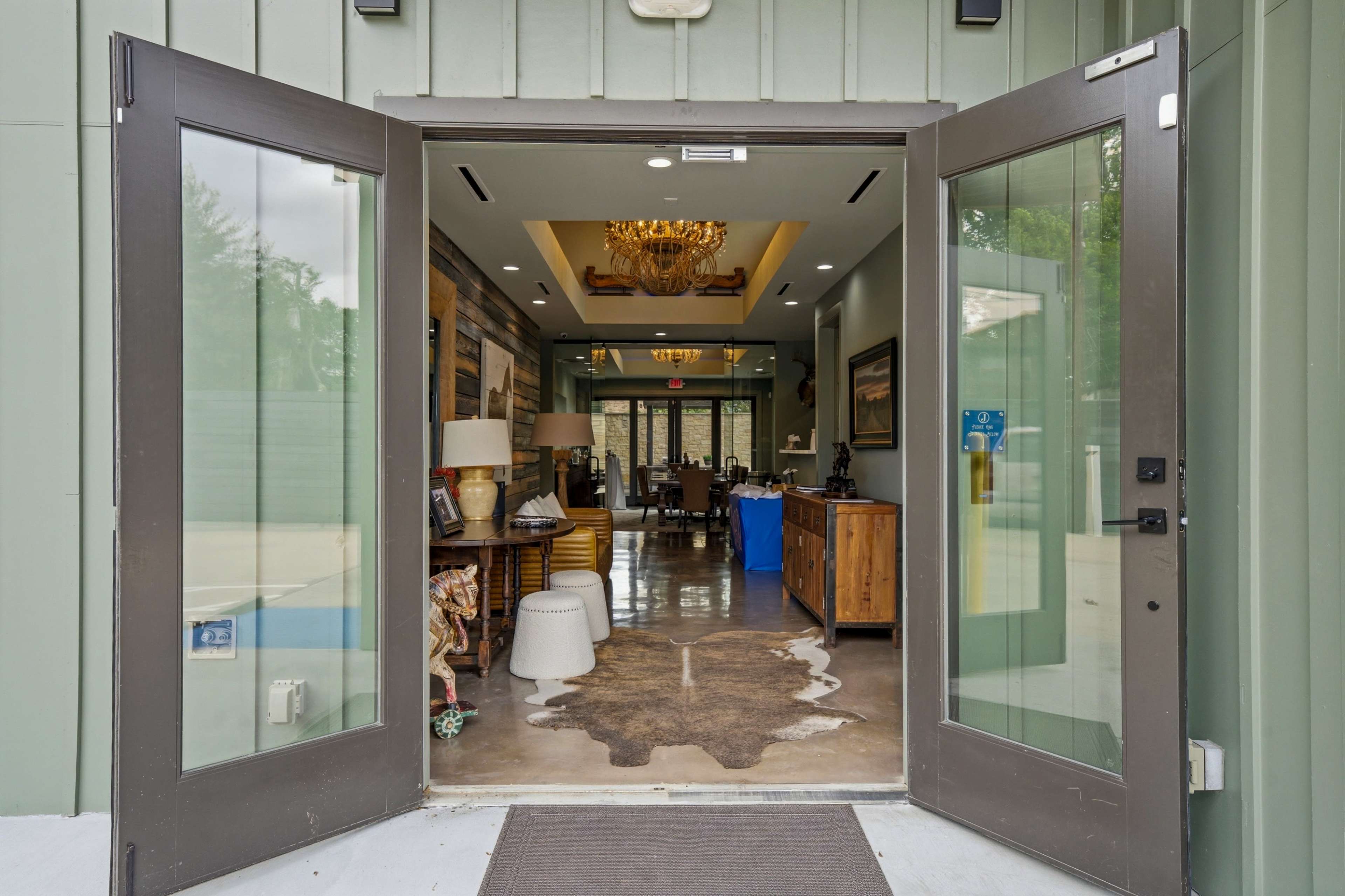 The image shows an open set of double doors leading into a well-decorated reception area with wooden furniture and a chandelier.