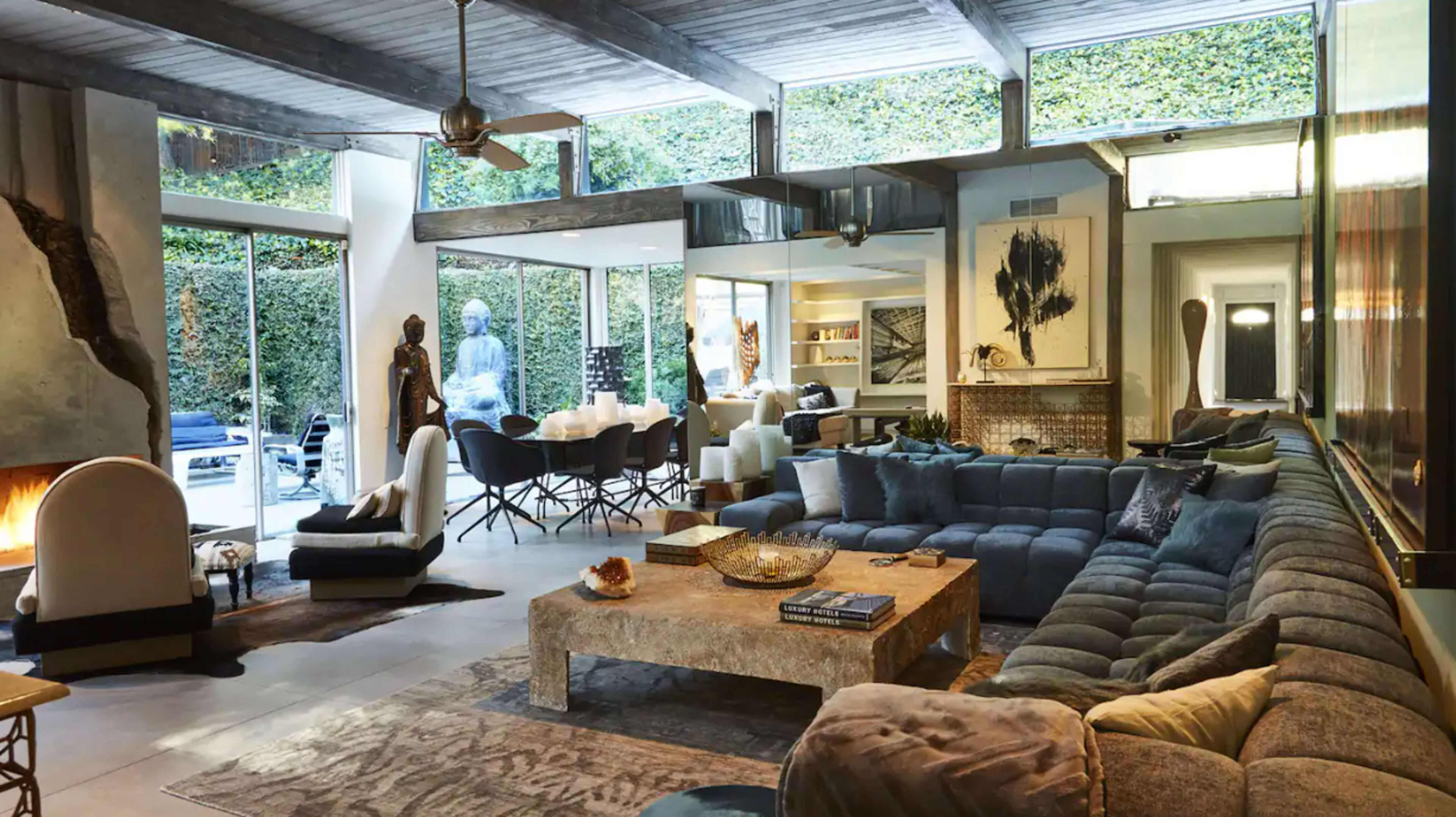 The image shows a modern living room with a large sectional sofa, a stone coffee table, and large windows allowing natural light to fill the space.