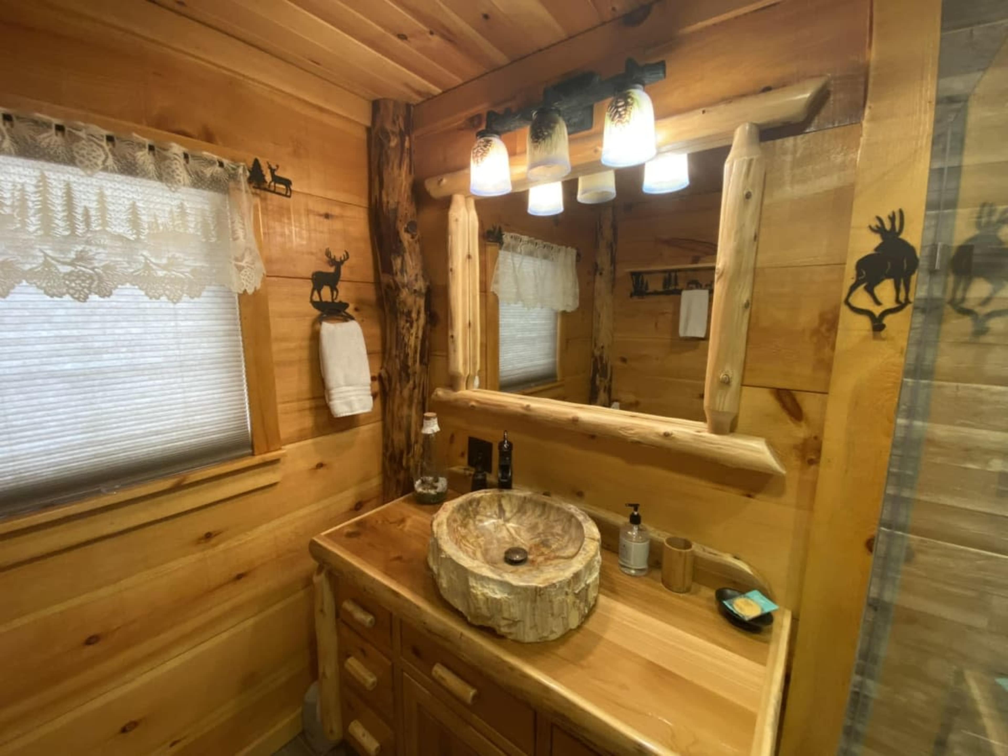 A rustic bathroom with wooden walls, a stone sink, and a mirror framed by a log, illuminated by three pendant lights.