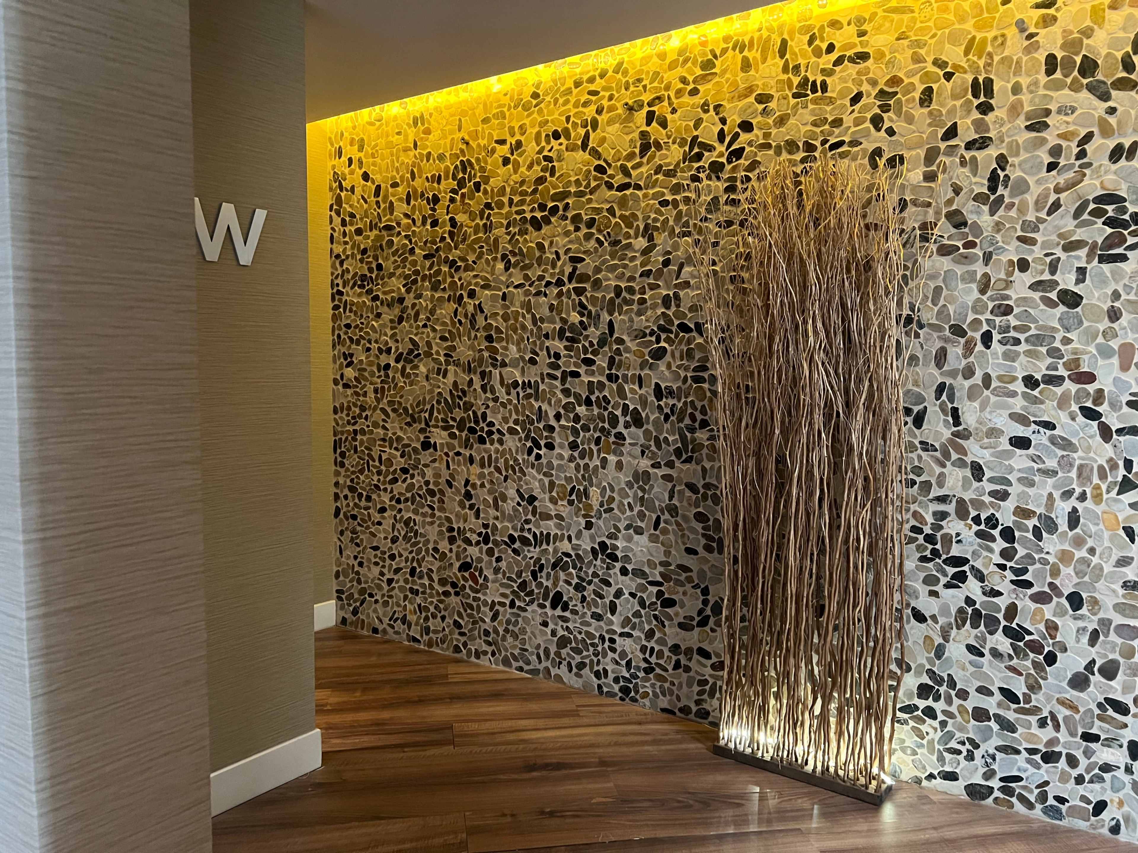 A textured stone wall is illuminated by warm lighting, accompanied by a decorative arrangement of tall, dry branches in a corner.