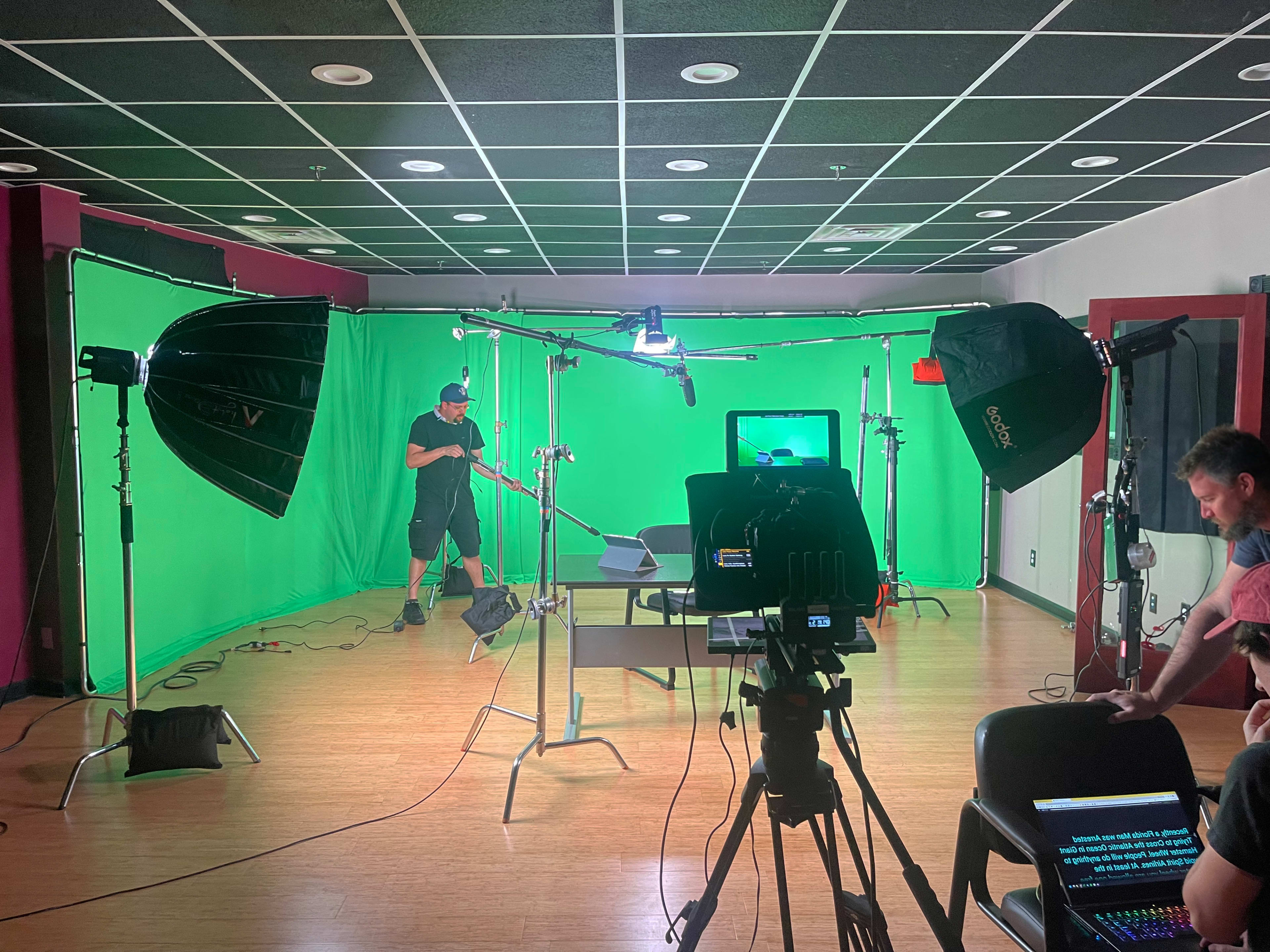 A video production studio is set up with green screens, lighting equipment, and a camera focused on a table.