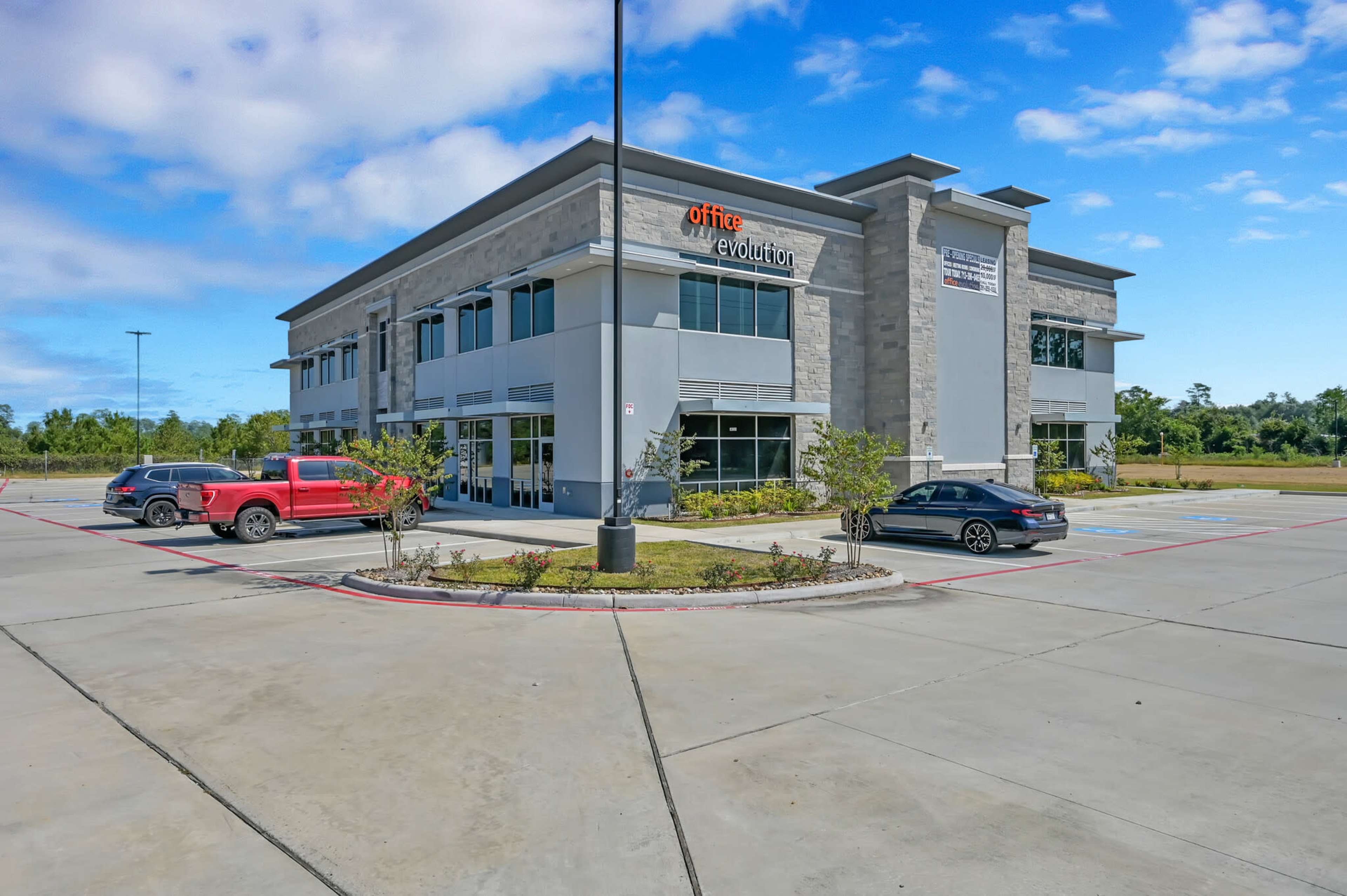 A modern two-story office building with a stone facade and large windows, surrounded by a paved parking lot.