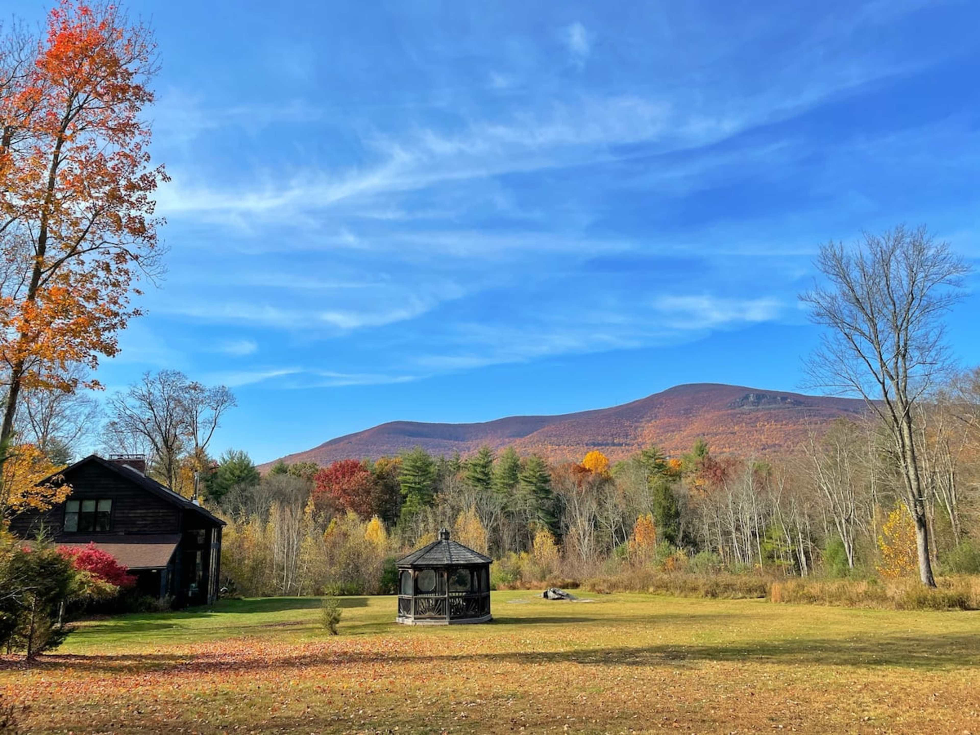 A black house with a gazebo is set against a backdrop of colorful autumn trees and mountains under a clear blue sky.