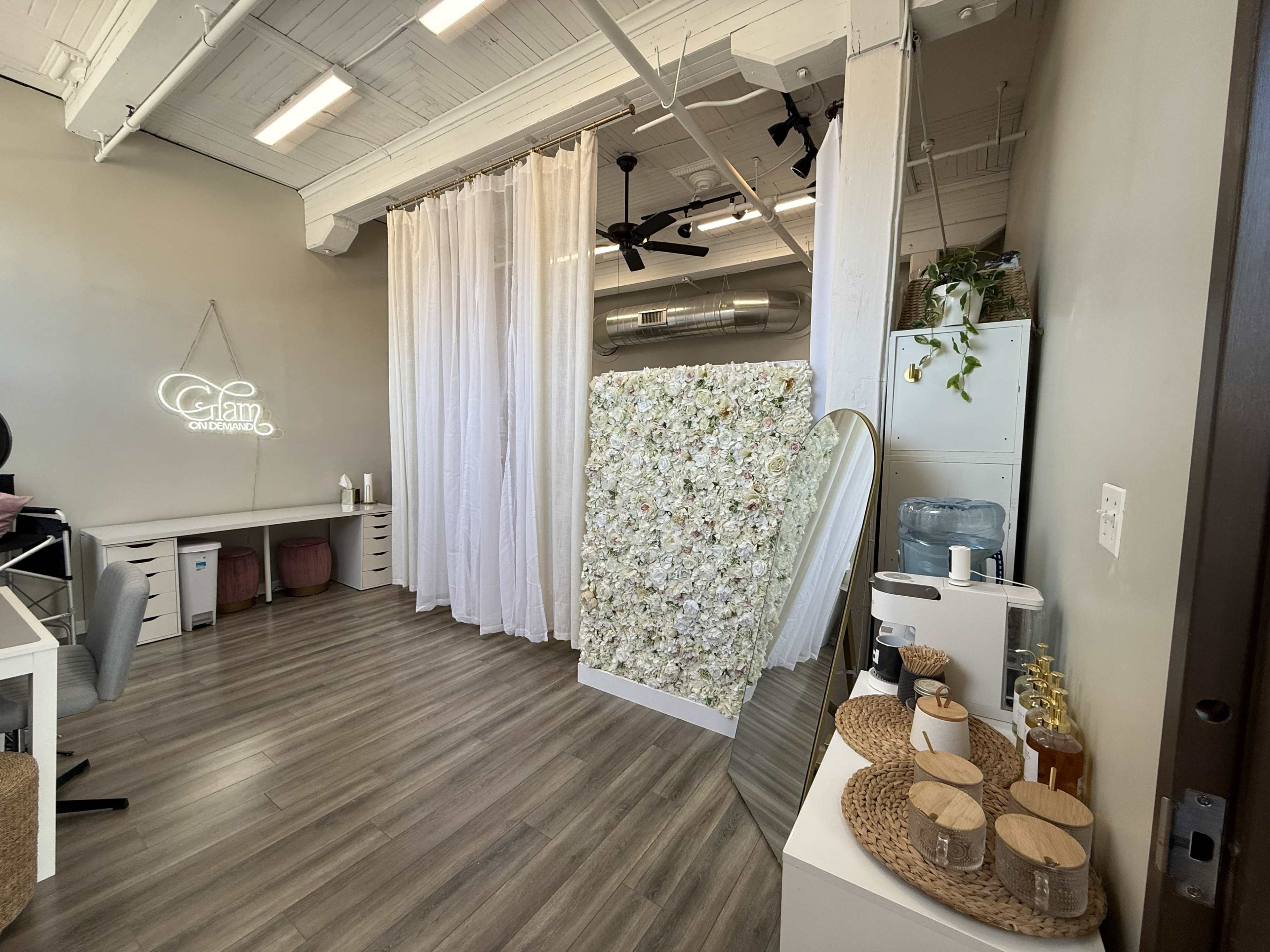 The image shows an interior of a beauty salon featuring a floral wall, a large mirror, and a water cooler, with white curtains dividing the space.