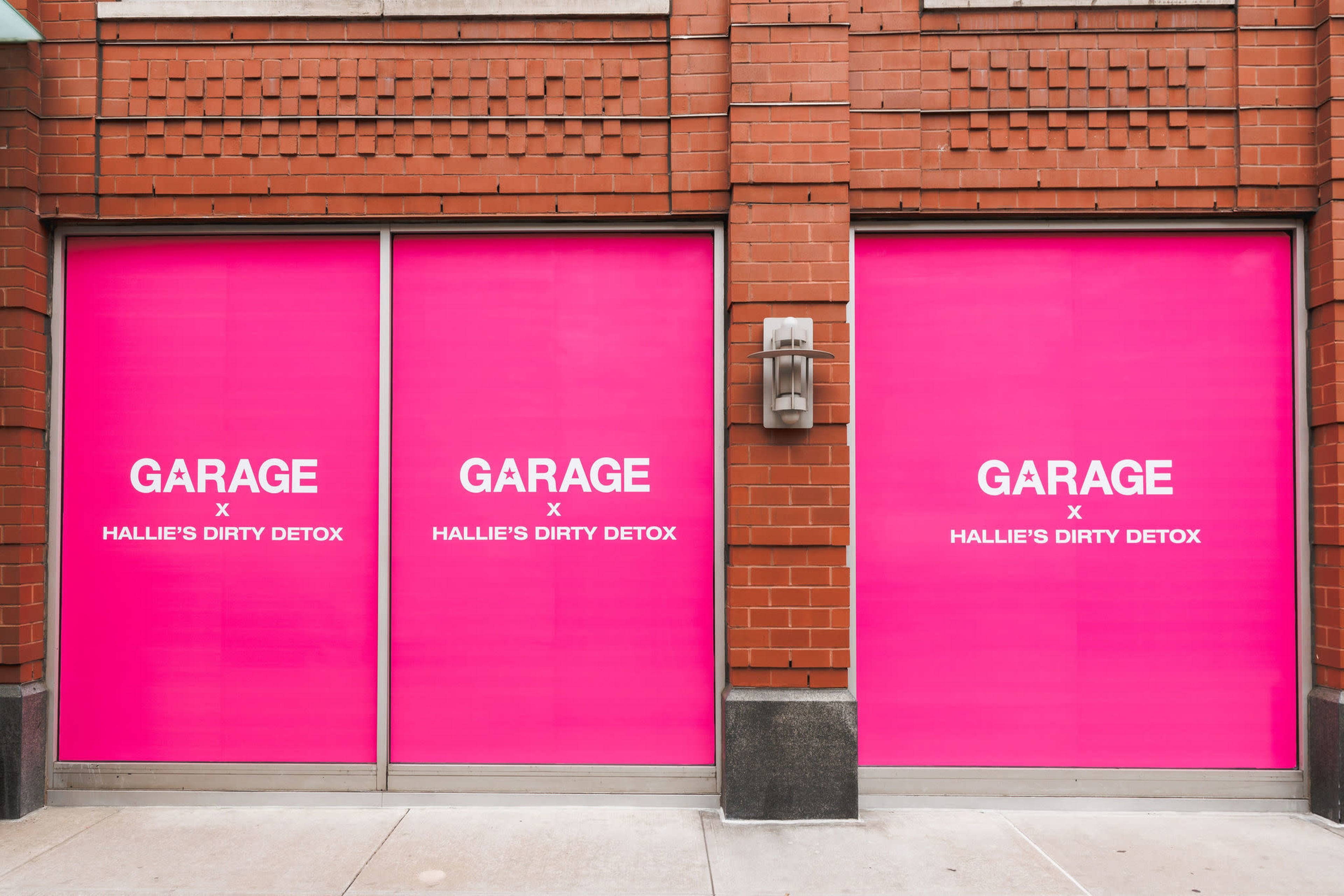 The image shows two large windows covered with bright pink signage displaying the text "GARAGE x HALLIE'S DIRTY DETOX."