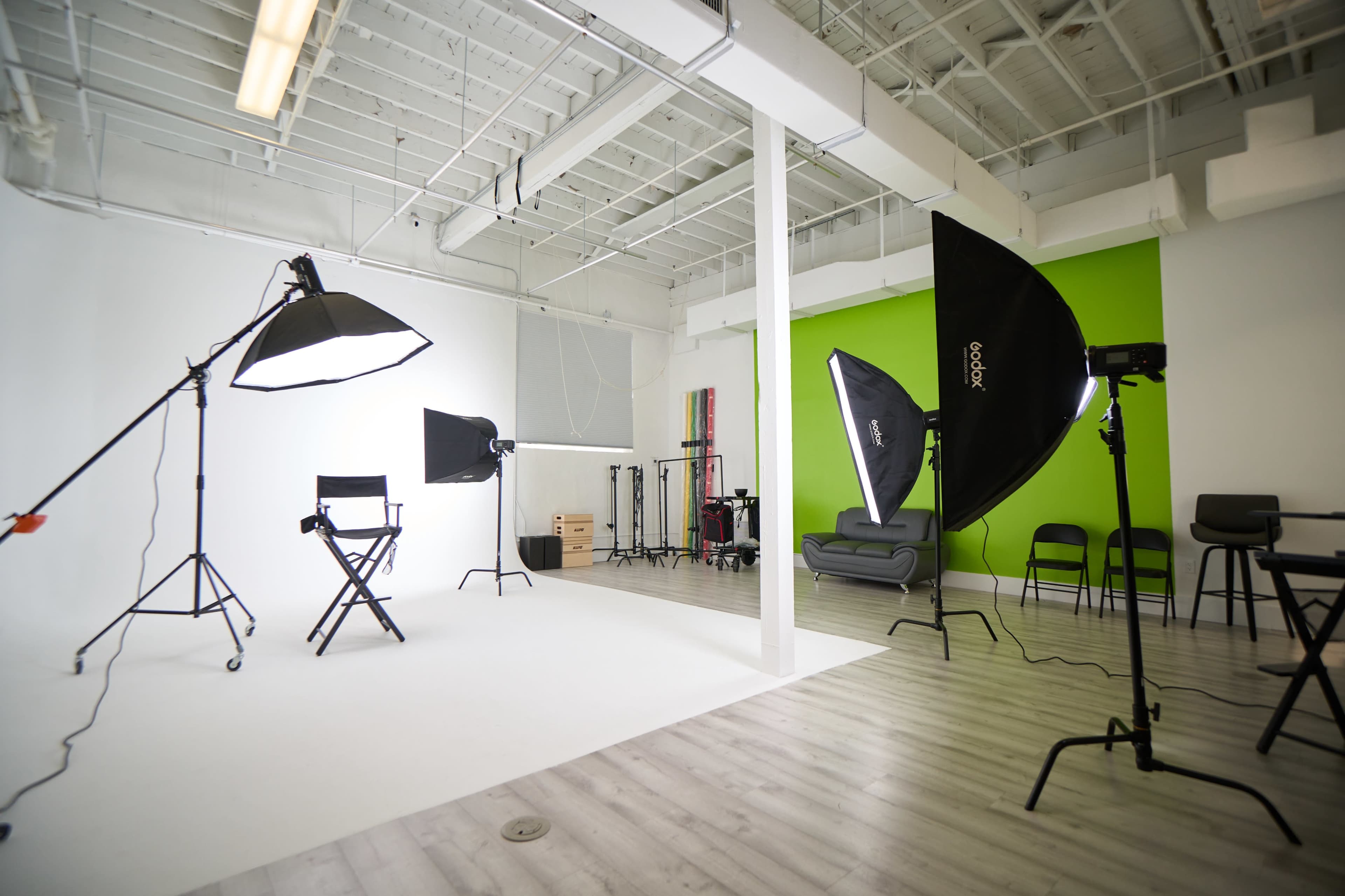 A photography studio with various lighting equipment, a director's chair, and a green accent wall.