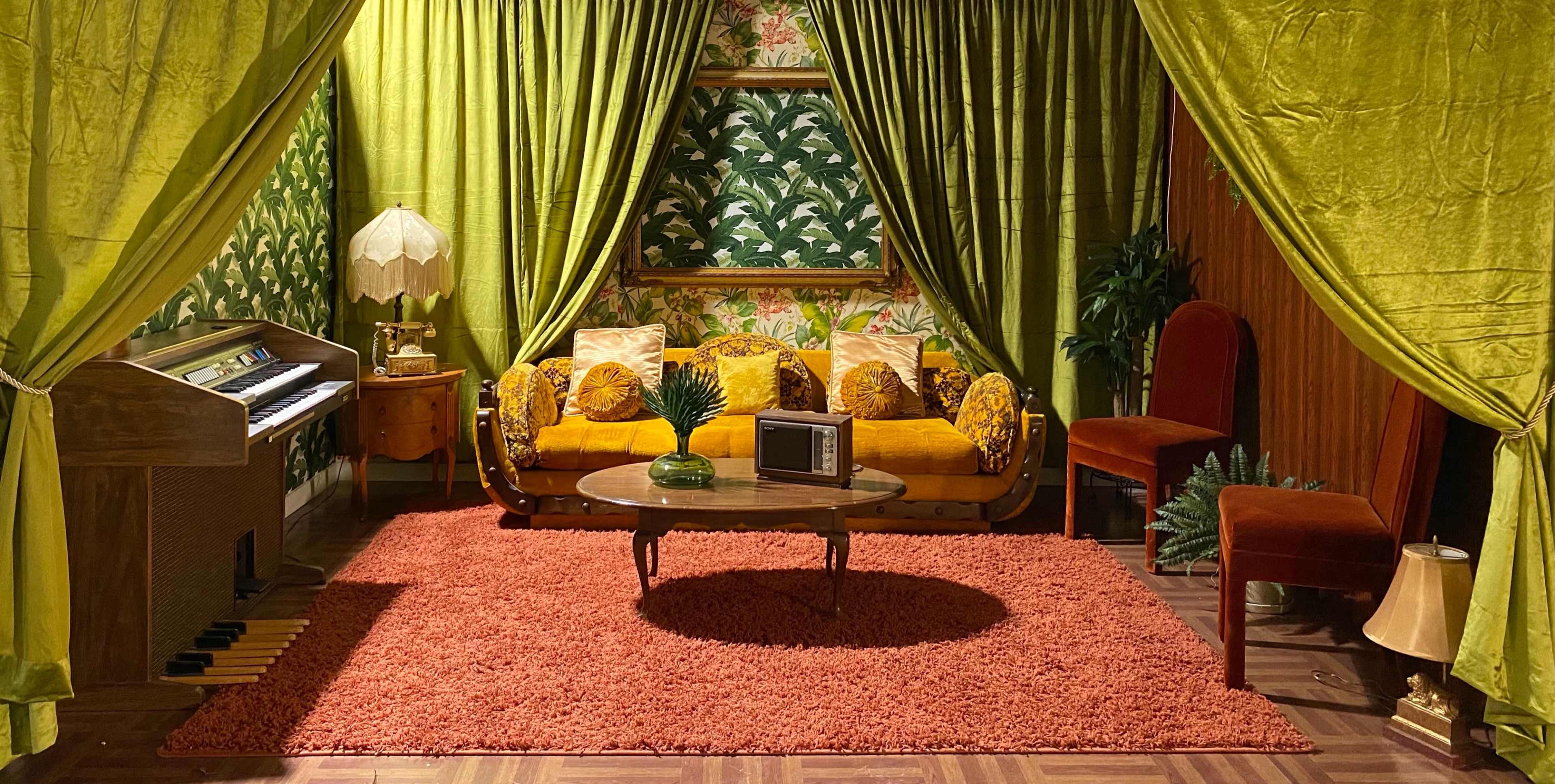 A vintage-themed living room with a green curtain backdrop, a sofa adorned with yellow floral patterns, a round coffee table, and a retro television set.