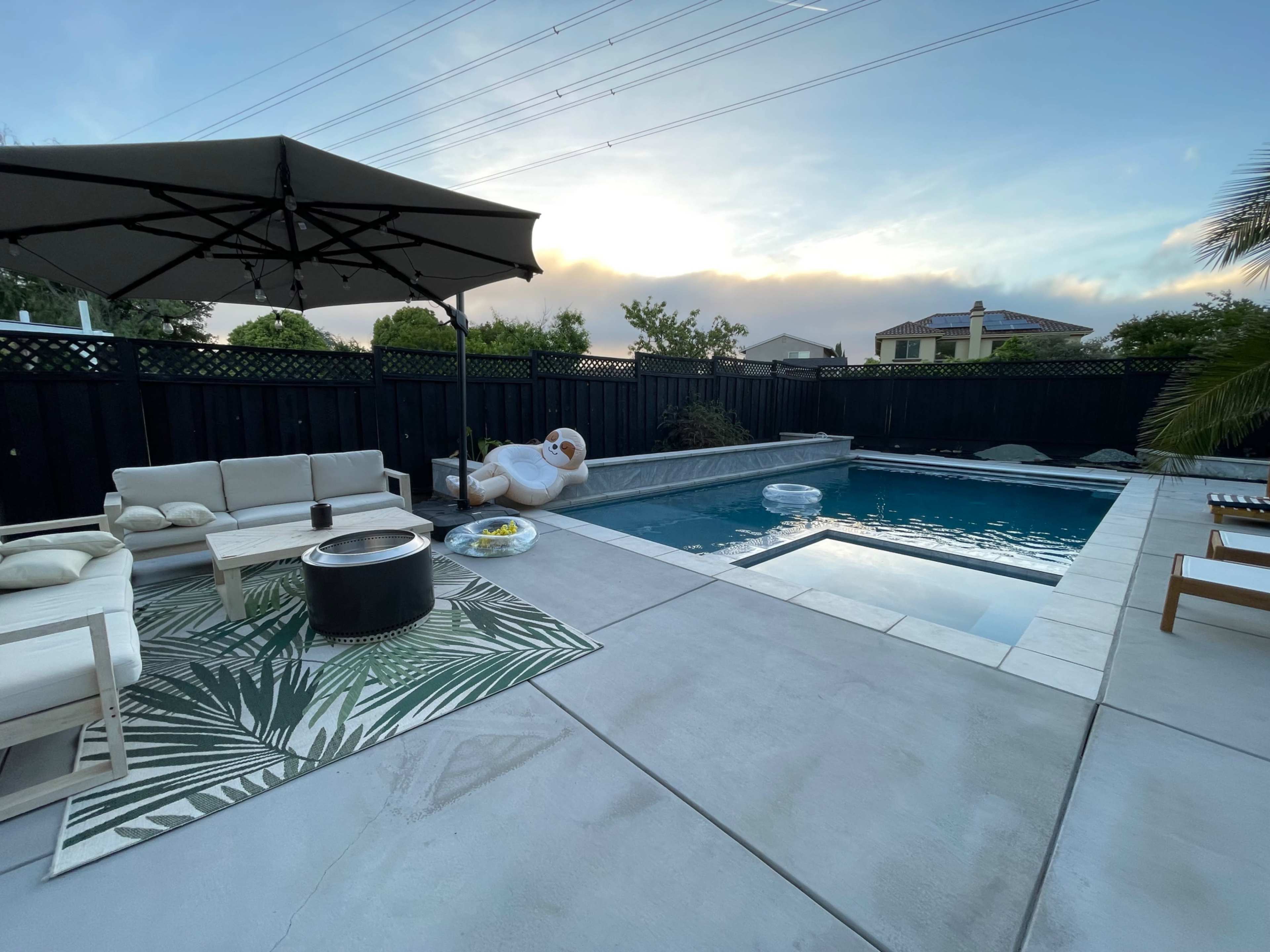 A modern backyard with a swimming pool, patio seating under an umbrella, and a floating inflatable in the water.