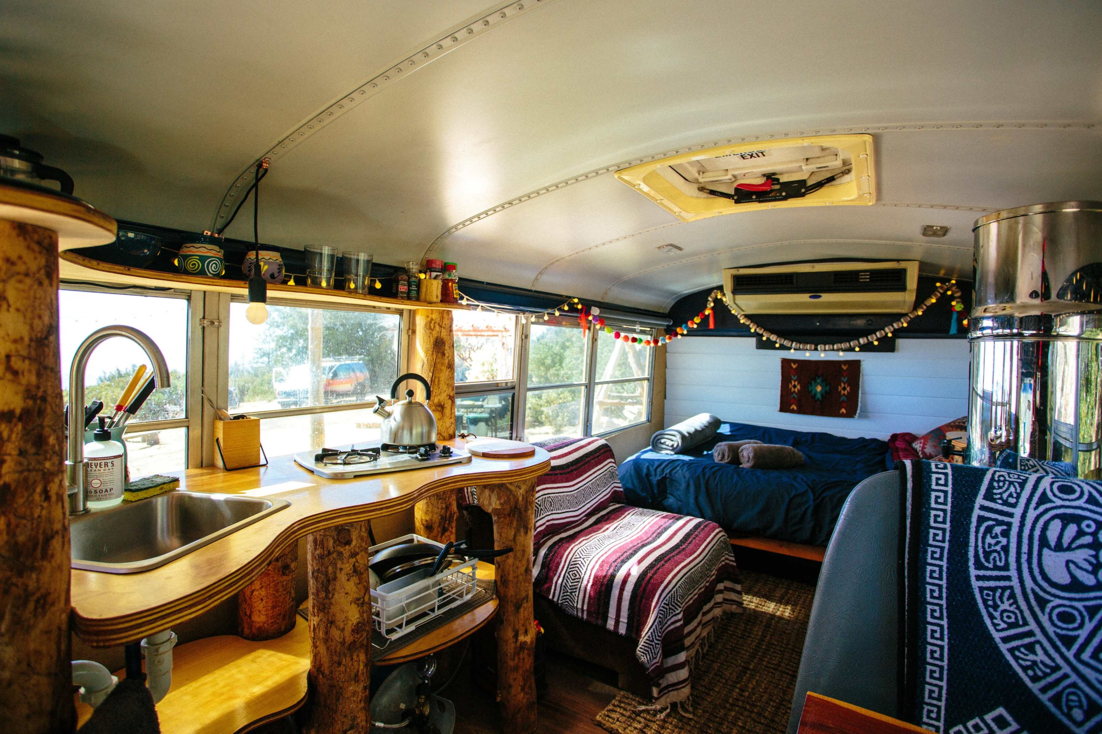 The interior of a renovated bus, featuring a kitchen area with a sink and stove, two beds, and decorative lighting.