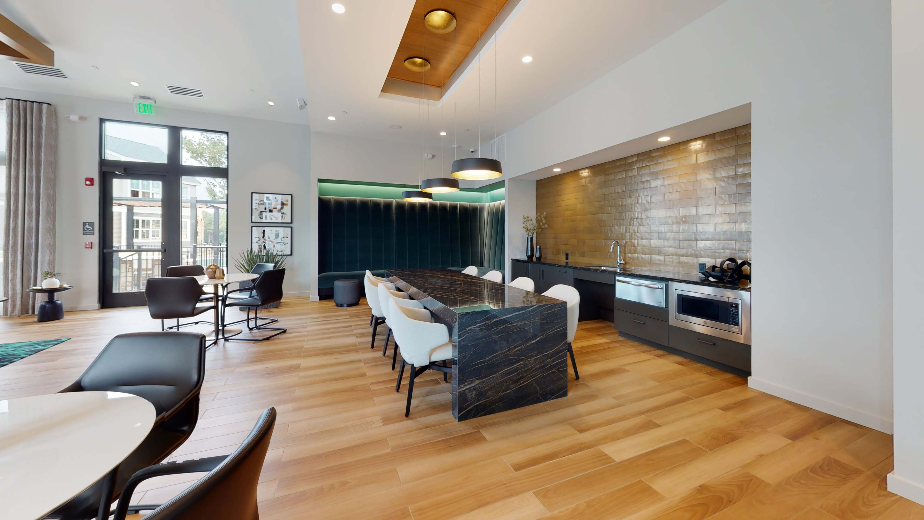 A modern kitchen and dining area features a long marble table surrounded by stylish chairs, with sleek appliances and large windows letting in natural light.