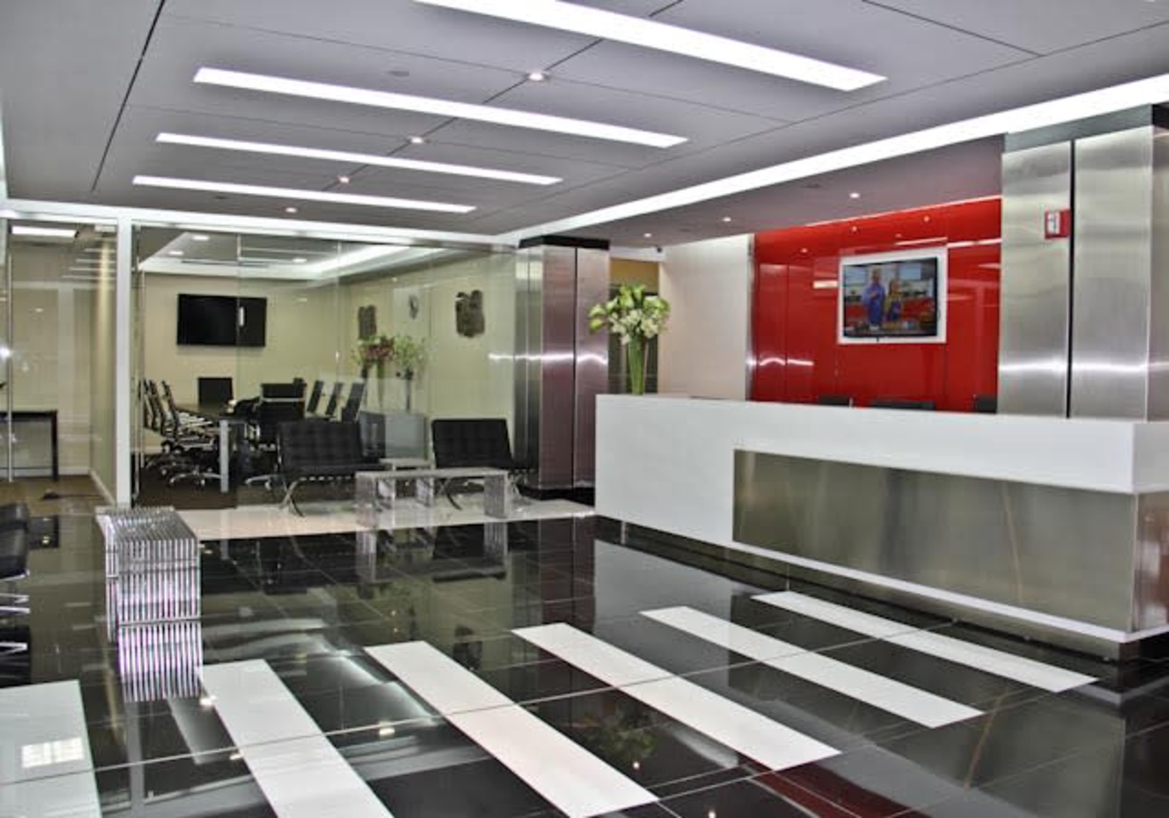 A modern office reception area features a sleek white front desk, a polished black and white tile floor, and a glass-walled conference room in the background.