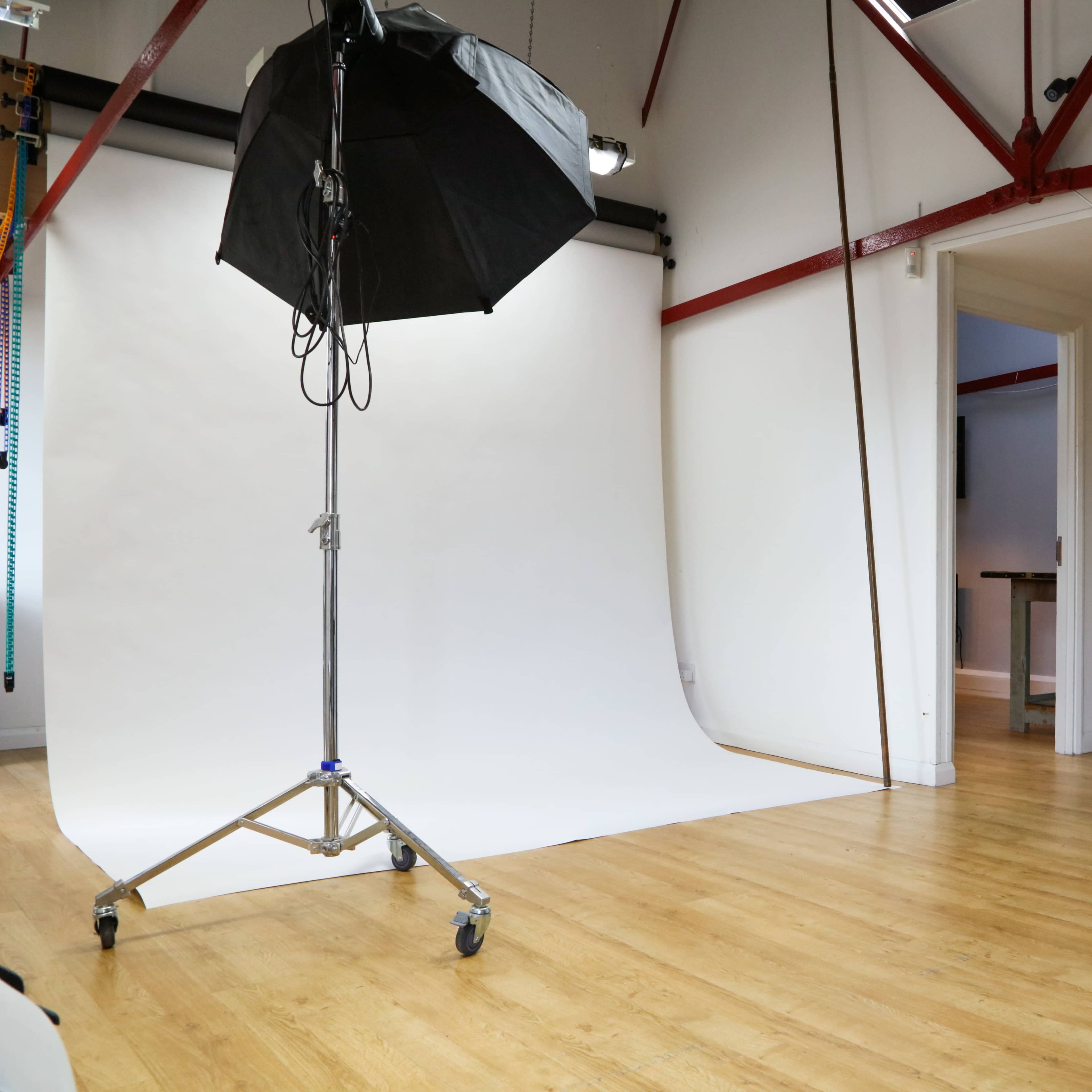 A photography studio with a white backdrop, a lighting setup on a stand, and wooden flooring.
