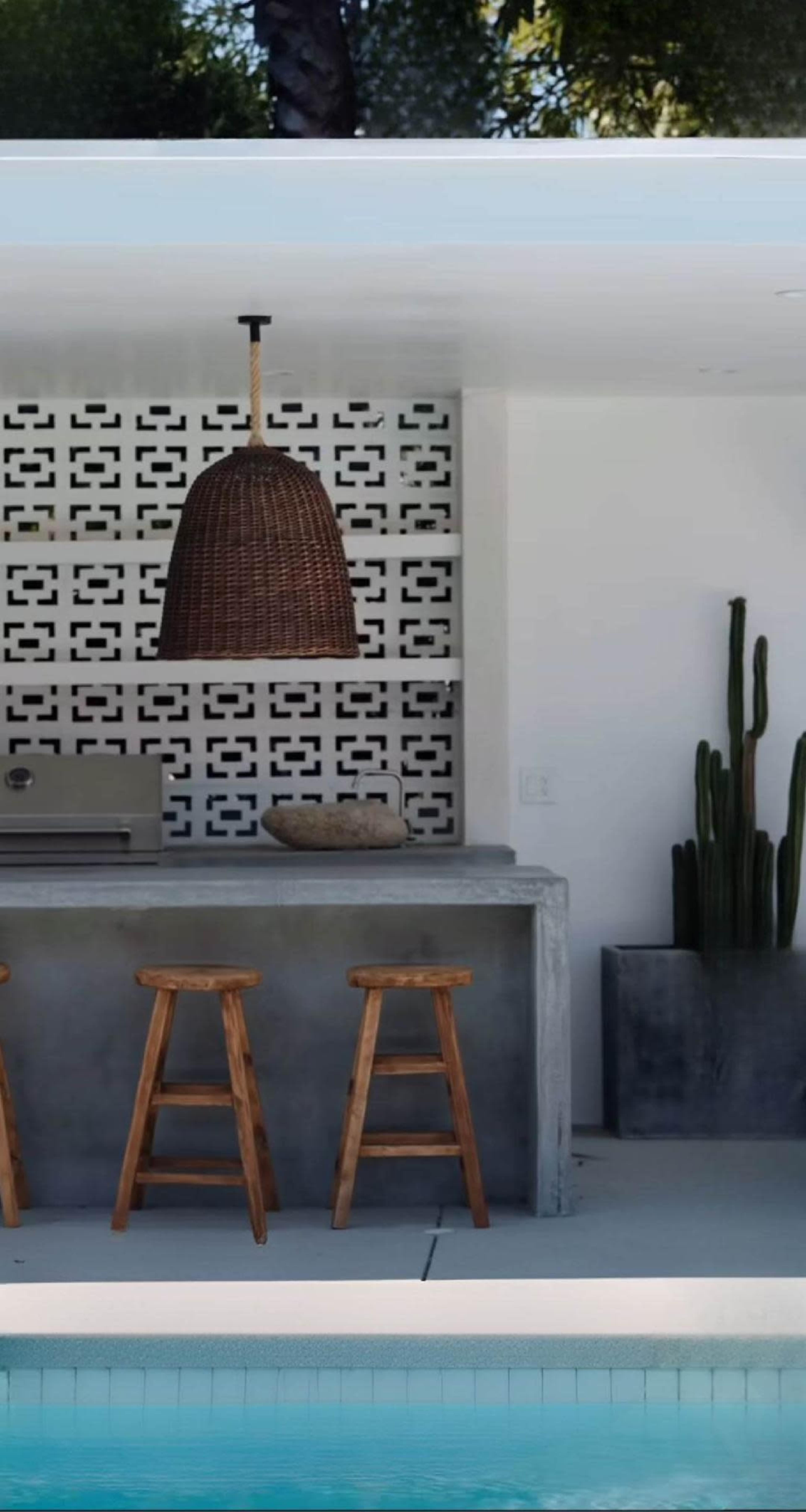 The image features a modern outdoor bar area with three wooden stools, a stone countertop, and a decorative wall with geometric patterns.