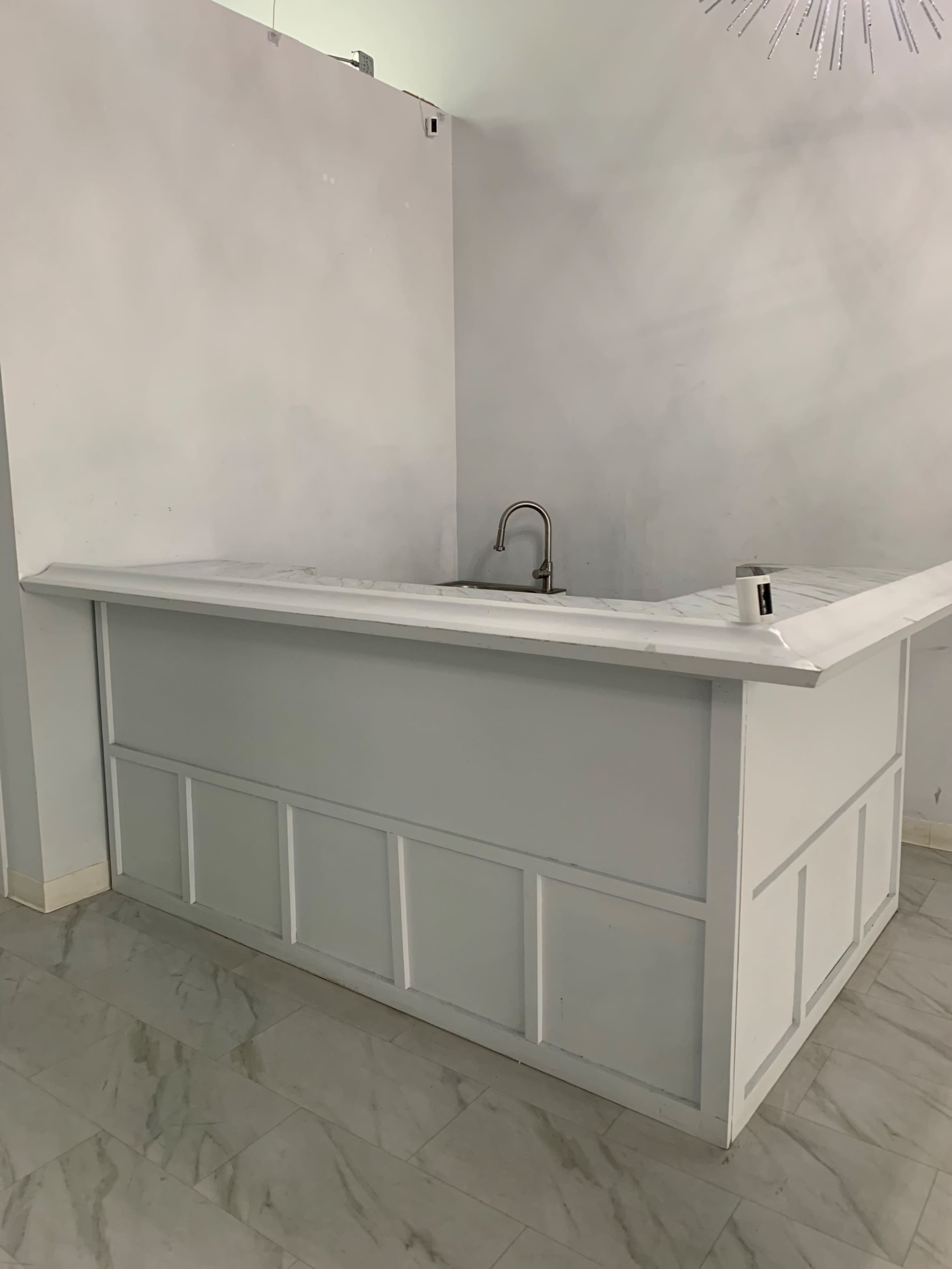 A white kitchen counter with a sink, set against a light-colored wall in a tile-floored room.