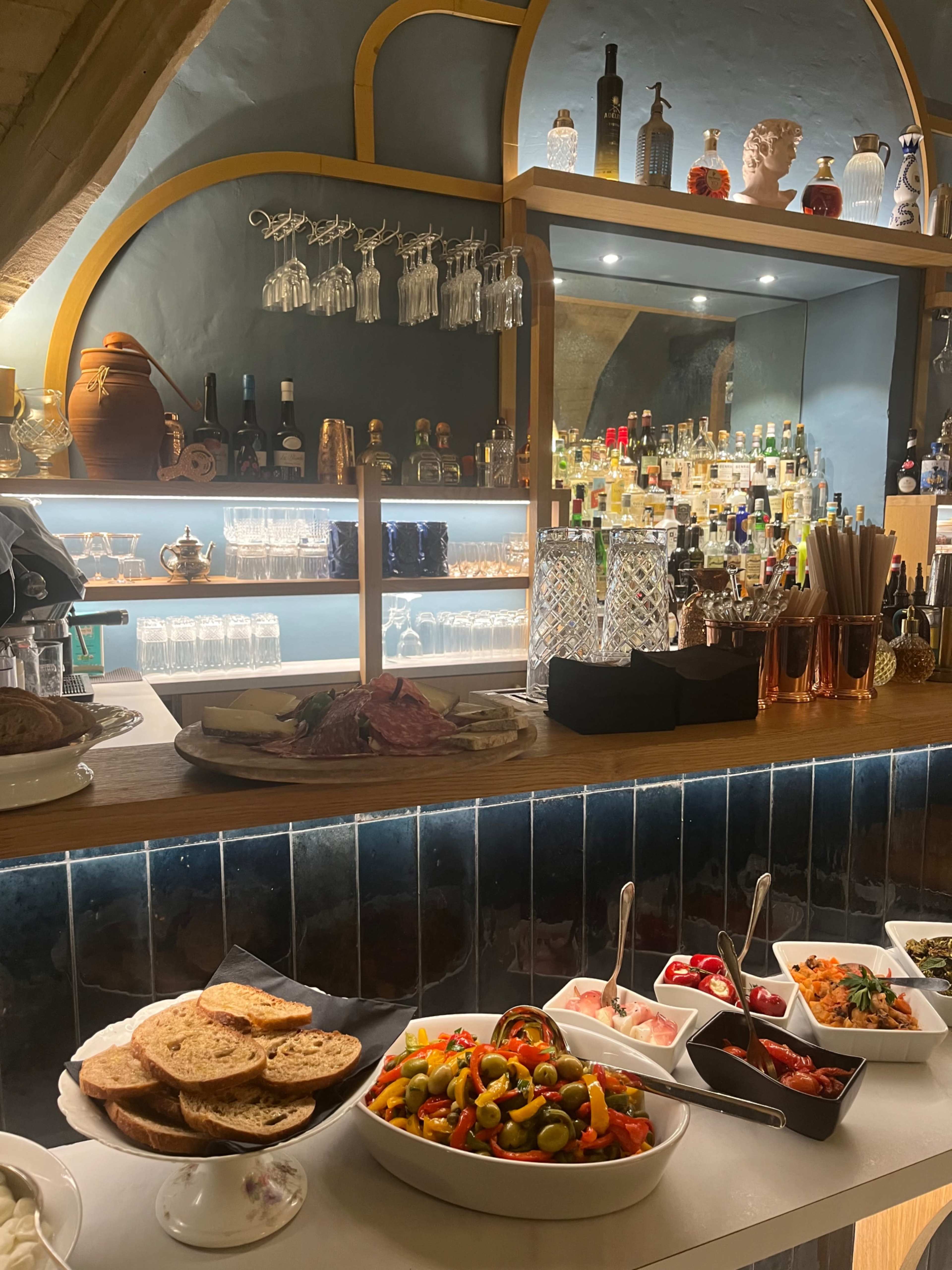 The image shows a well-arranged buffet table with various dishes and drinks displayed on a wooden counter topped with glassware and bottles.