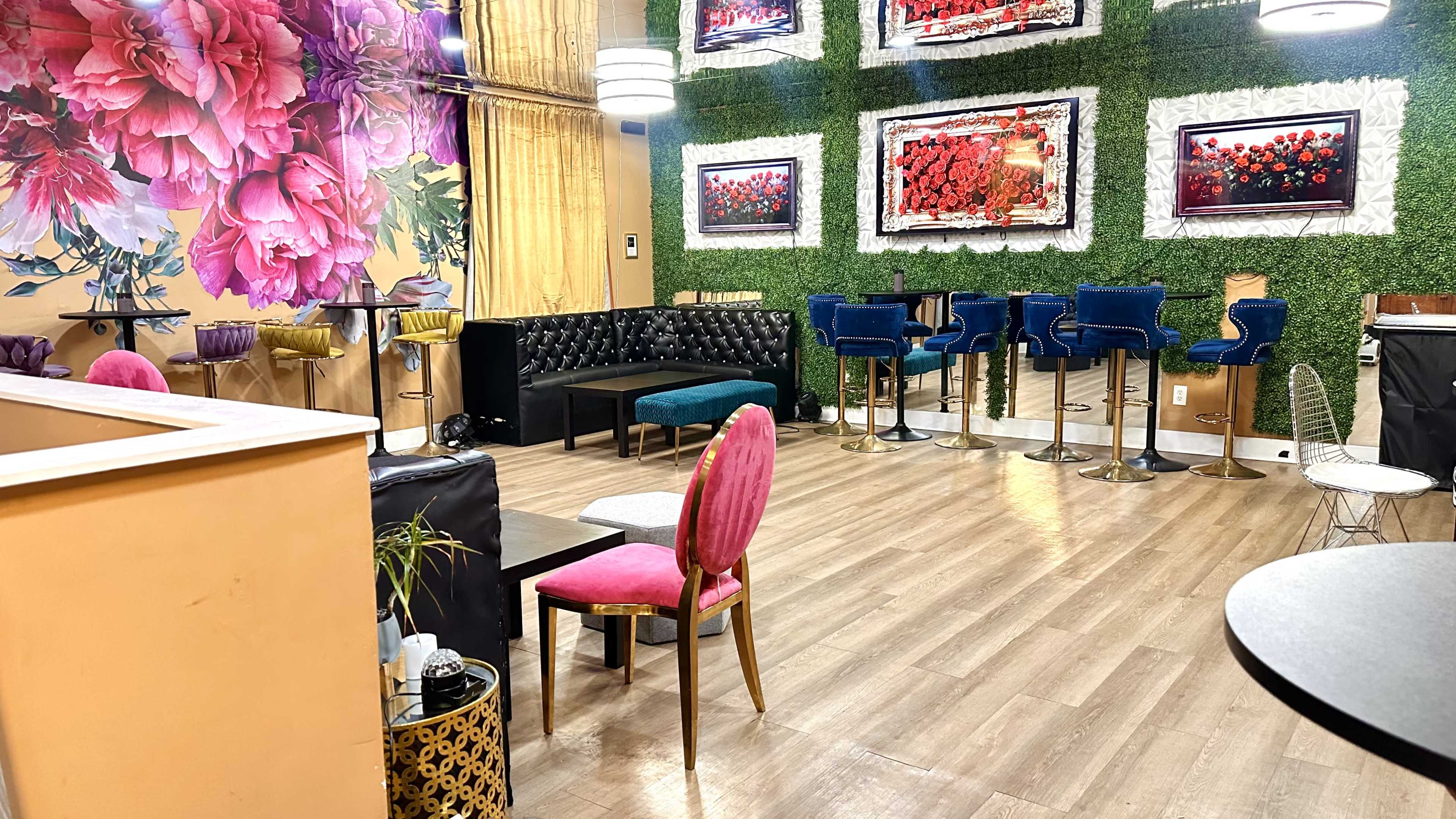 The image shows a stylish cafe interior featuring a floral mural, modern seating arrangements, and vibrant artwork on the walls.