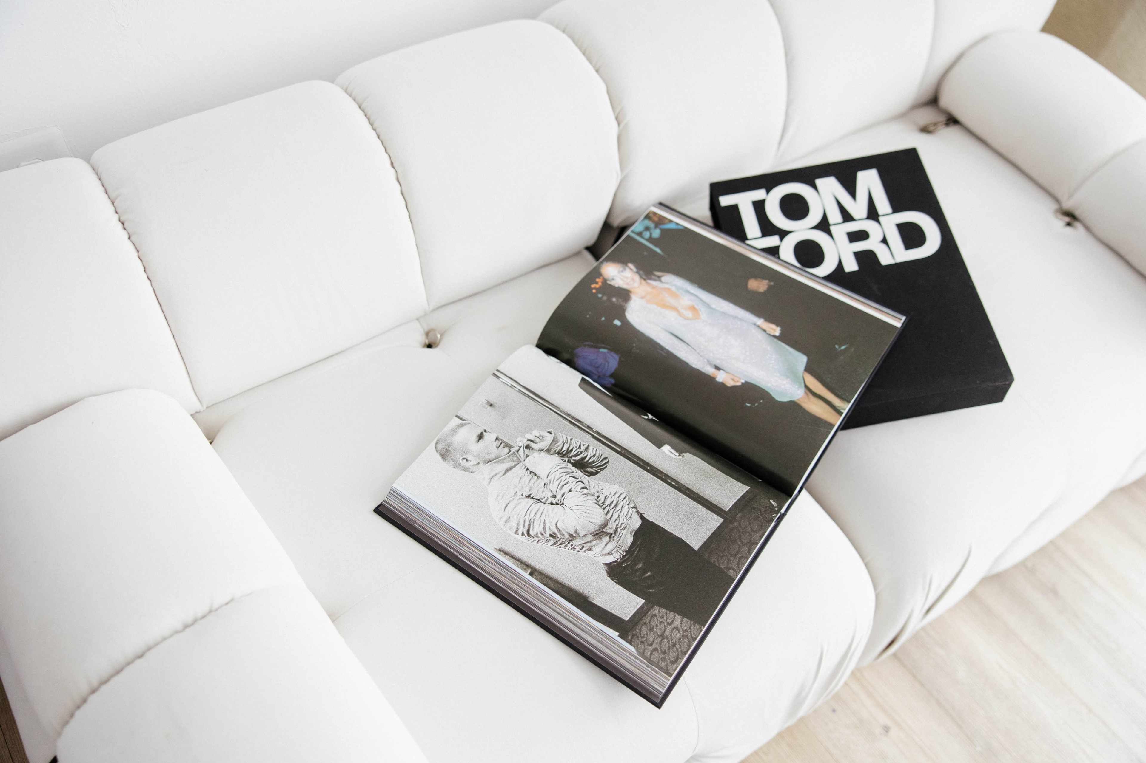 A white couch features an open fashion magazine and a black Tom Ford box on its surface.