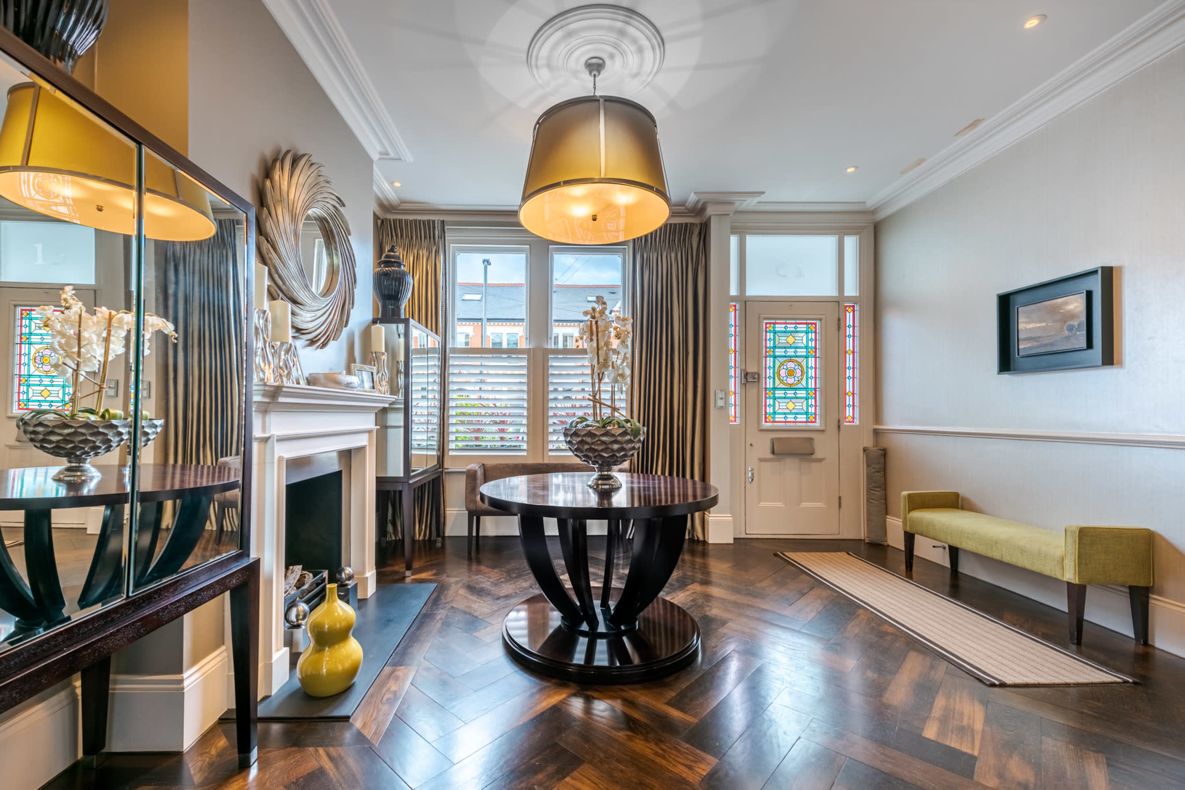 A stylish entryway featuring a round table, a large pendant light, a decorative mirror, and colorful stained glass windows.