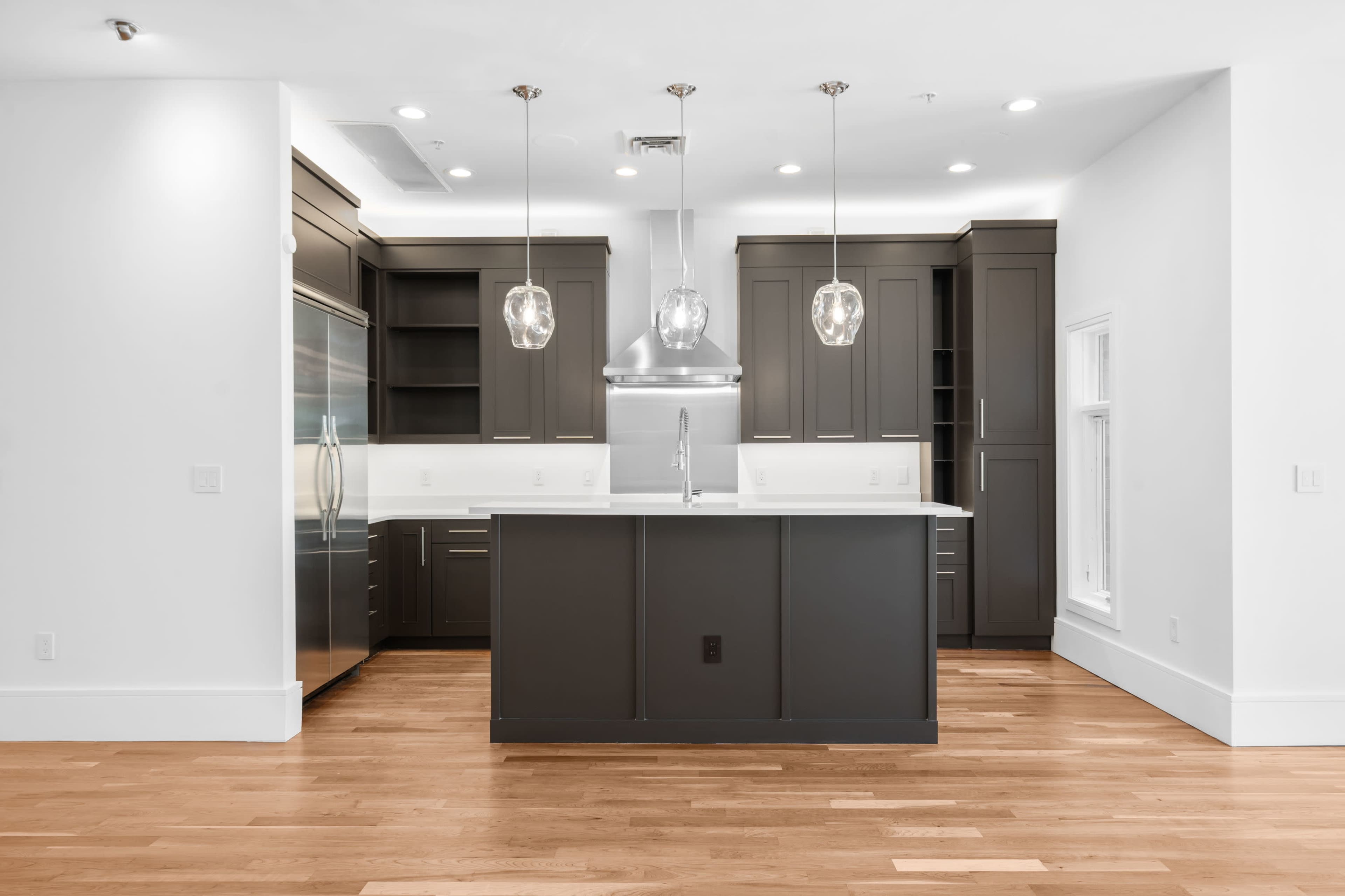 The image shows a modern kitchen featuring dark cabinetry, a central island with a white countertop, and pendant lighting above.