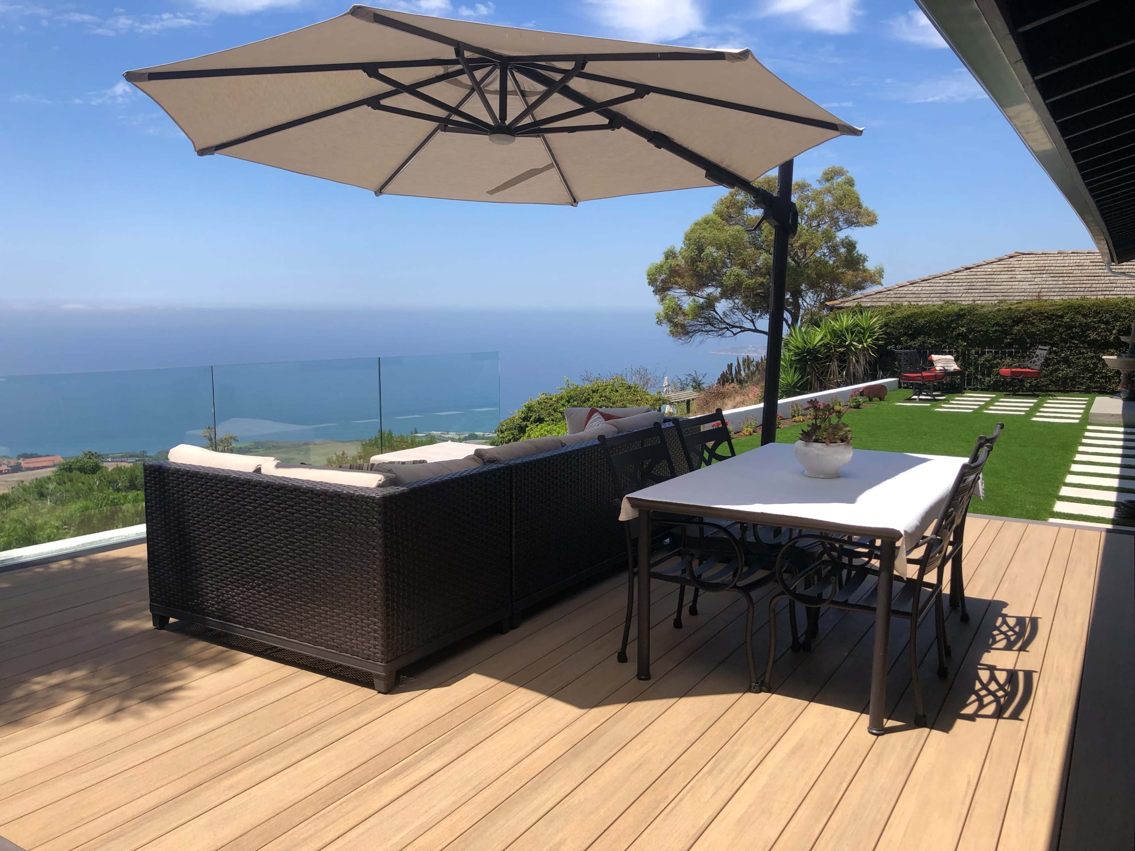 A patio with a sectional sofa, dining table, and large umbrella overlooks a scenic view of the ocean.