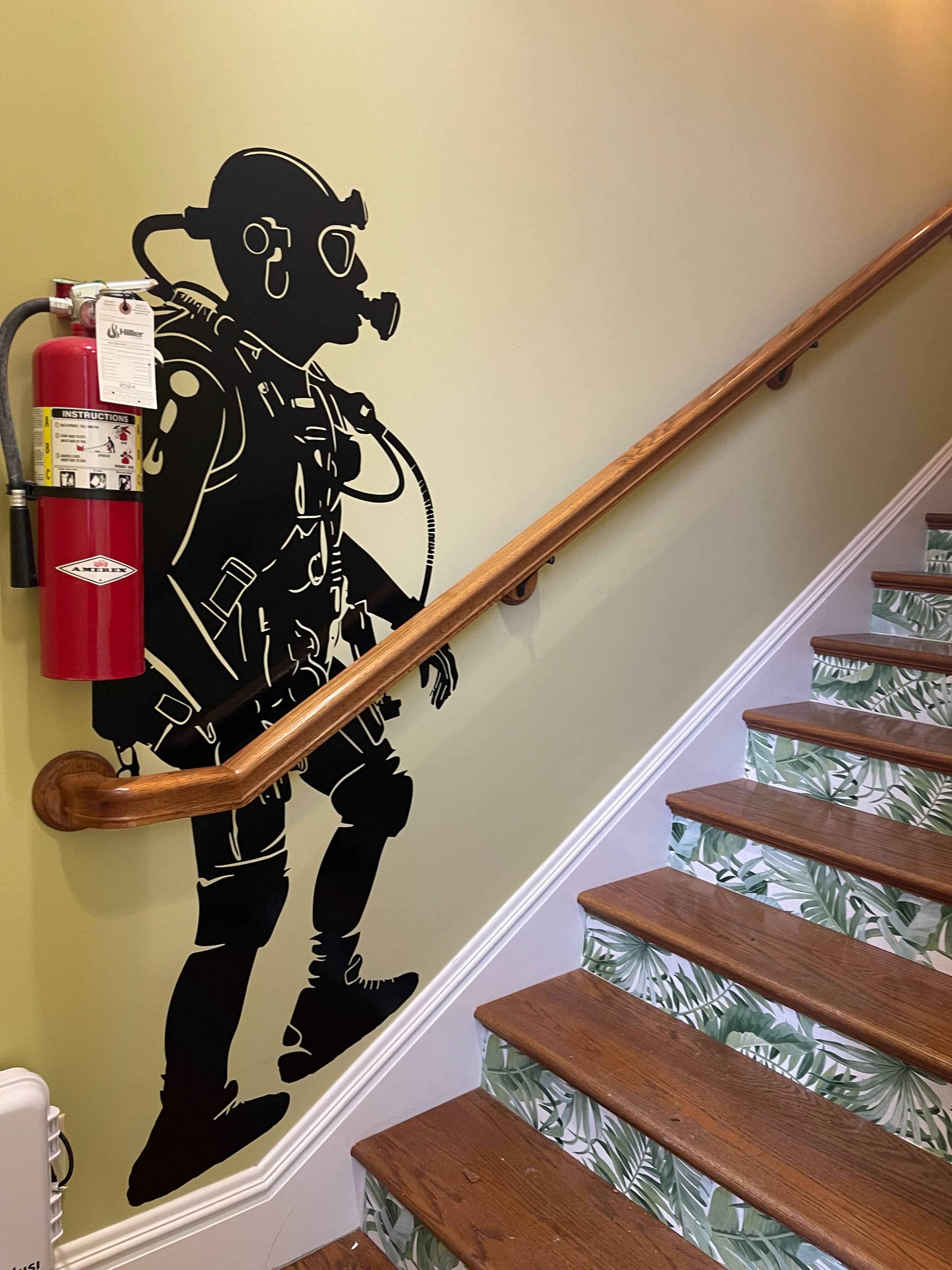 The image shows a staircase with a decorative wall mural of a diver in diving gear beside a fire extinguisher mounted on the wall.