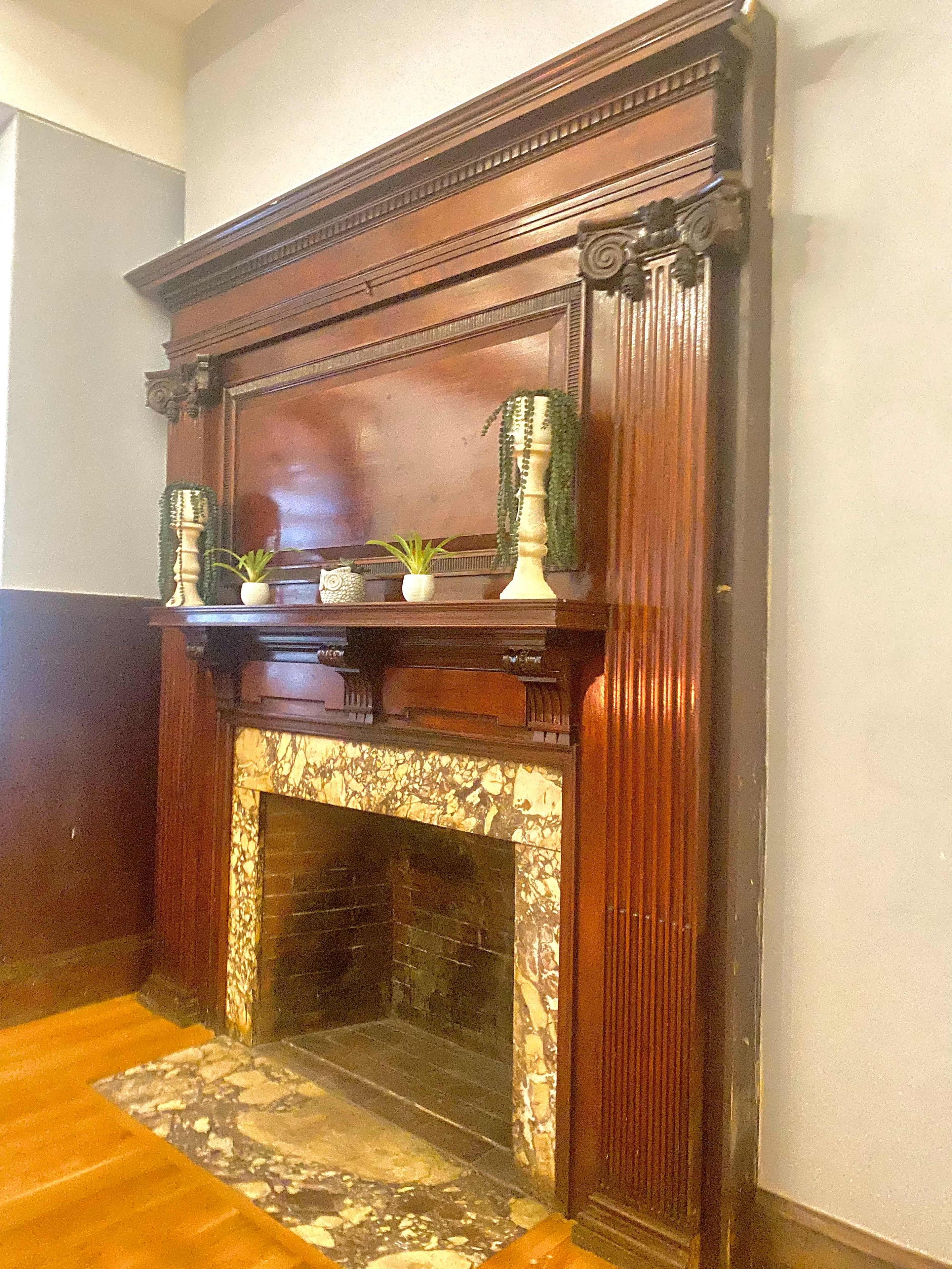 An ornate wooden fireplace with a marble surround, flanked by decorative lamps and small plants.