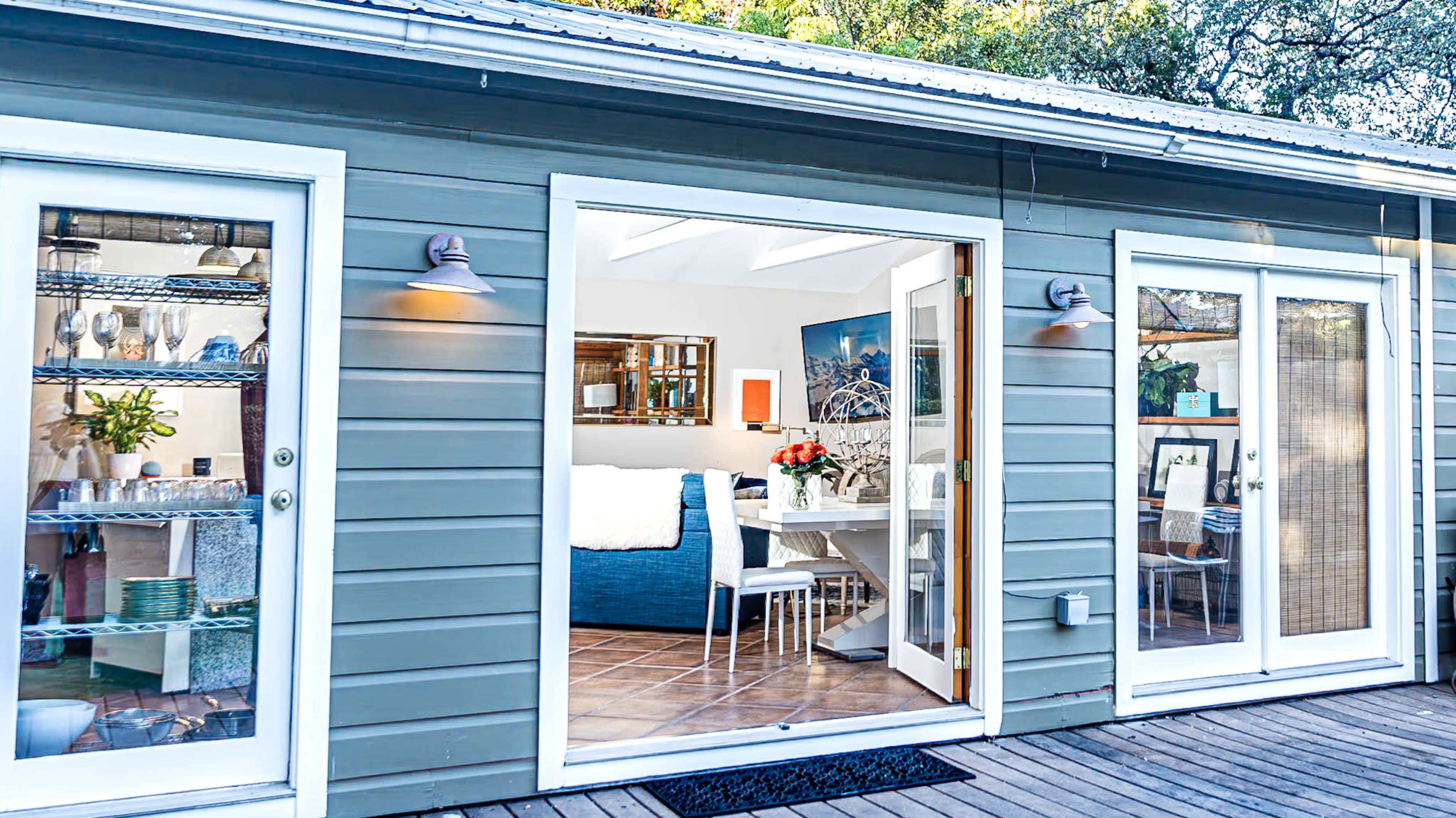 A modern gray house features open doors leading into a bright, cozy interior furnished with a dining table and decor.