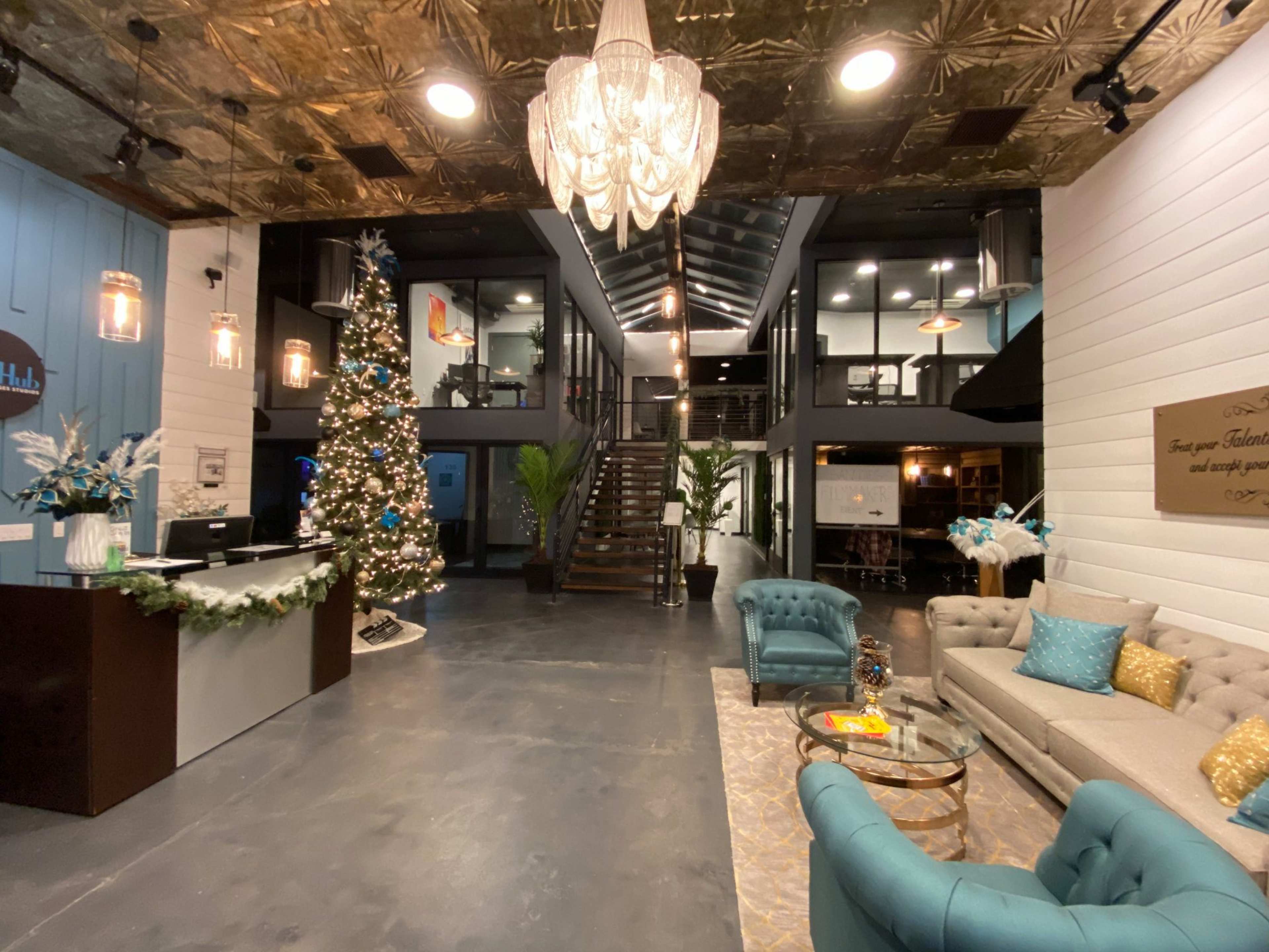 The image shows a modern lobby decorated for the holidays, featuring a Christmas tree, a reception desk, and seating areas with stylish furniture.