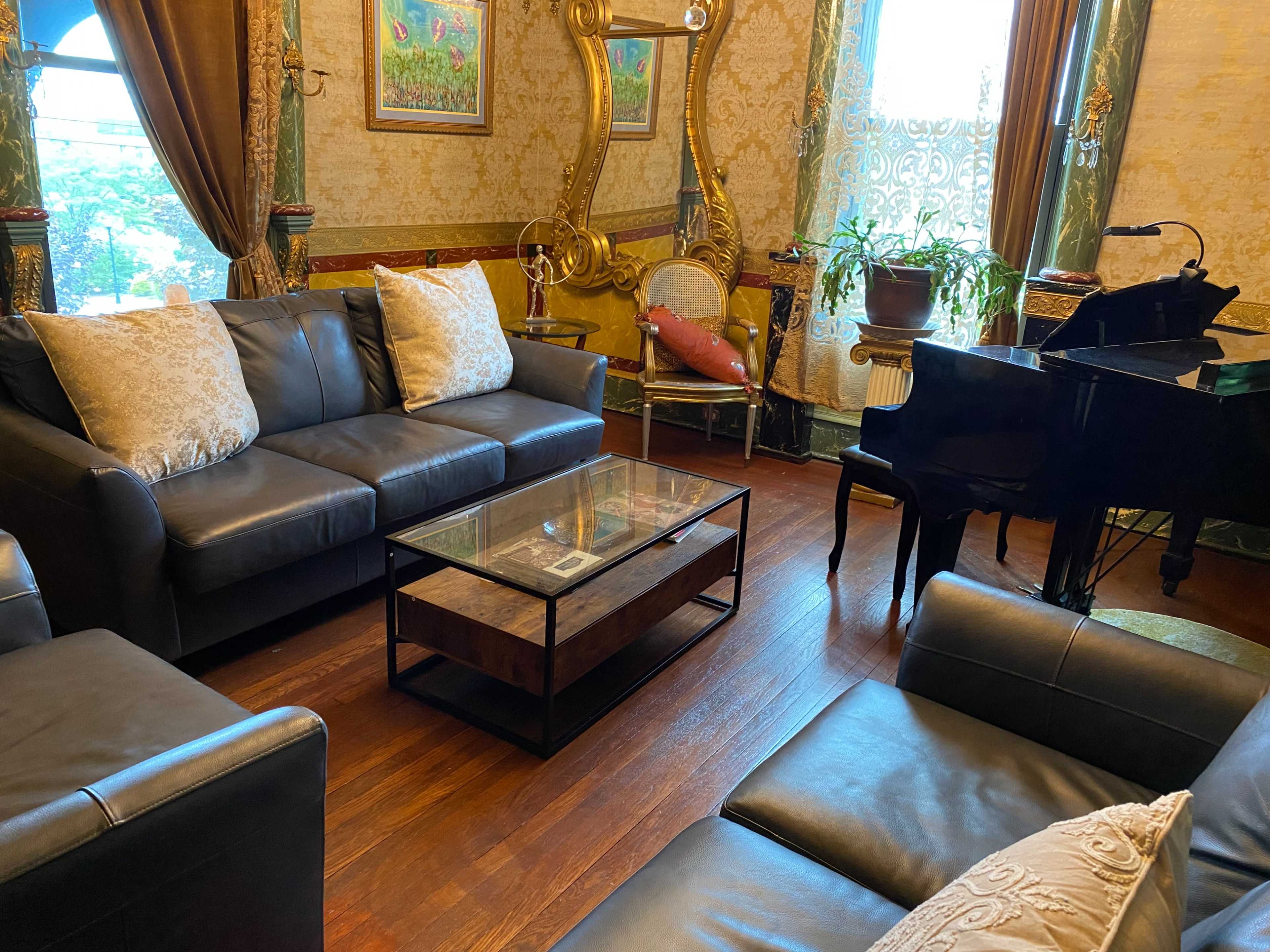 The image depicts a elegantly decorated living room featuring dark leather sofas, a glass coffee table, and a grand piano in the corner.