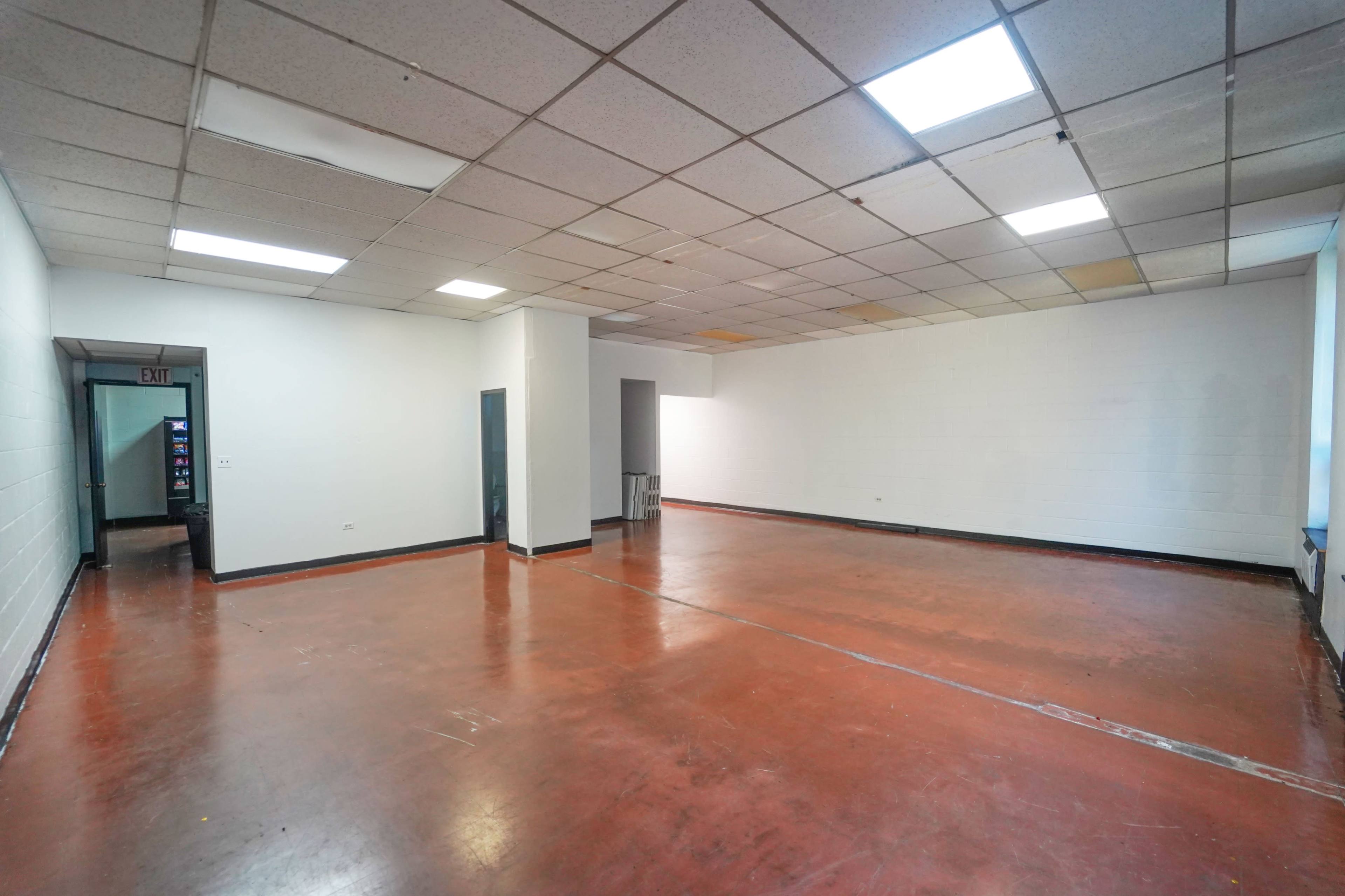 The image shows an empty, well-lit room with a red concrete floor and white walls, featuring two doorways.