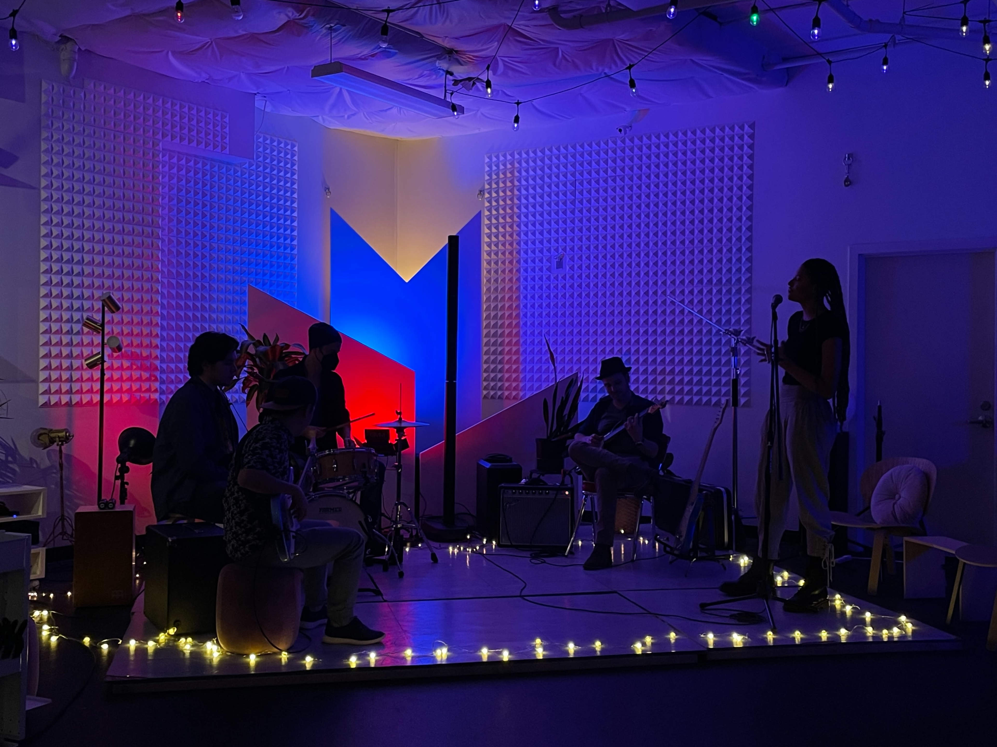 A band performs on a small stage adorned with colorful lights and ambient decorations.
