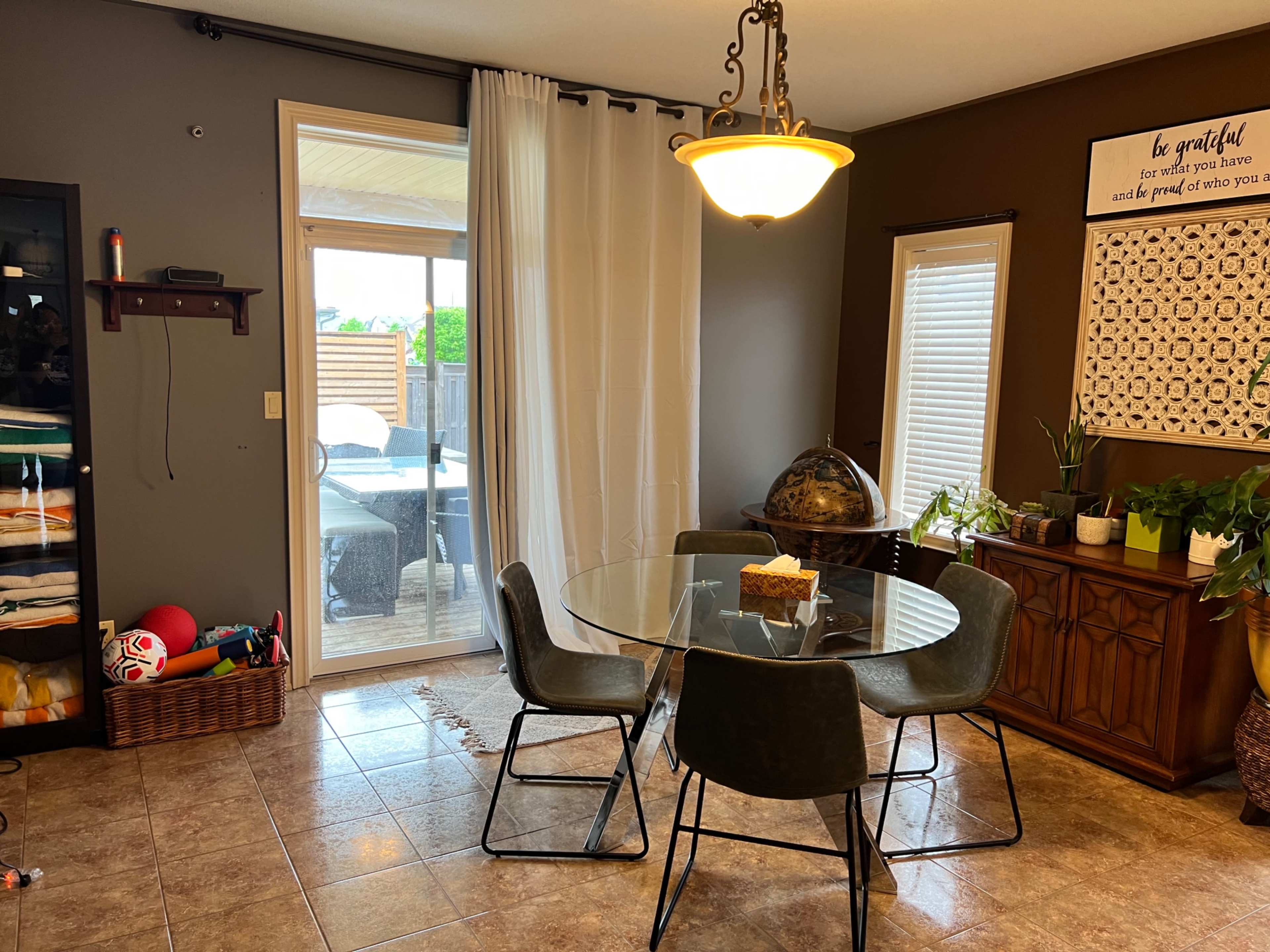 A round glass dining table with six chairs sits in a brightly lit dining area, adjacent to a sliding glass door leading to an outdoor space.