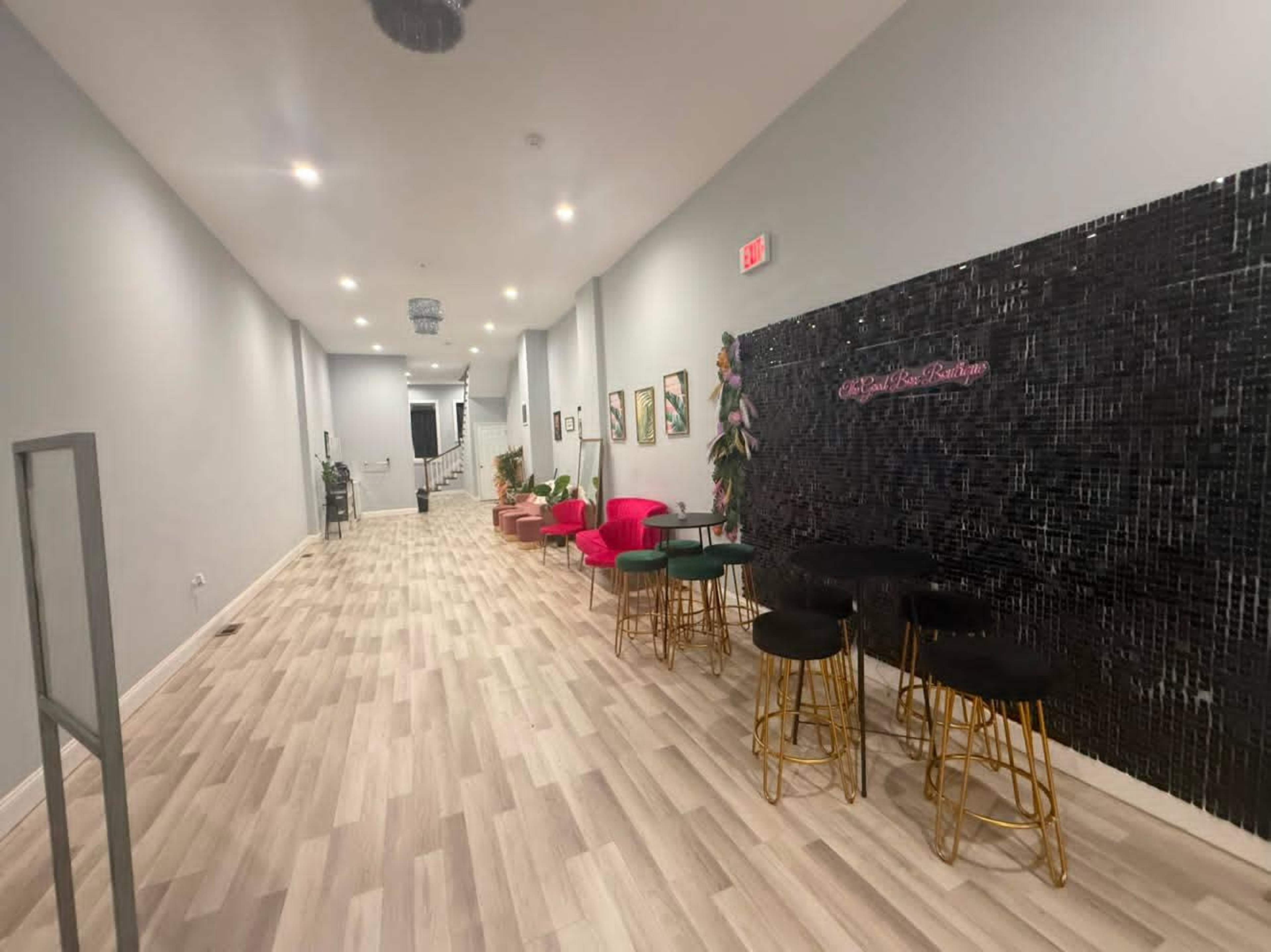 The image shows a long hallway with a glossy black feature wall and various seating arrangements, including pink chairs and black stools.