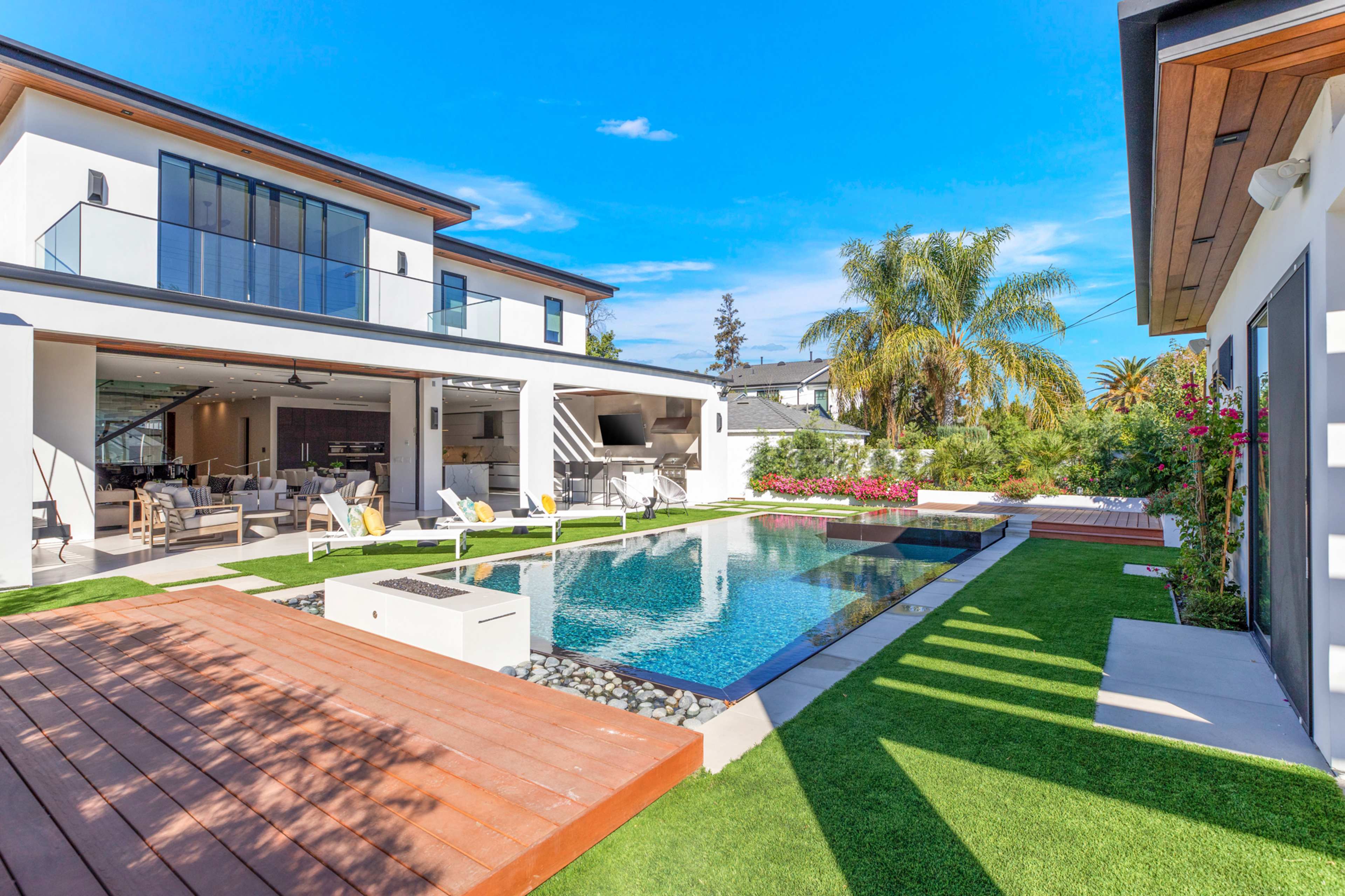A modern residential backyard featuring a large pool, surrounding lounge chairs, and a well-designed outdoor space with landscaped greenery and a two-story house.