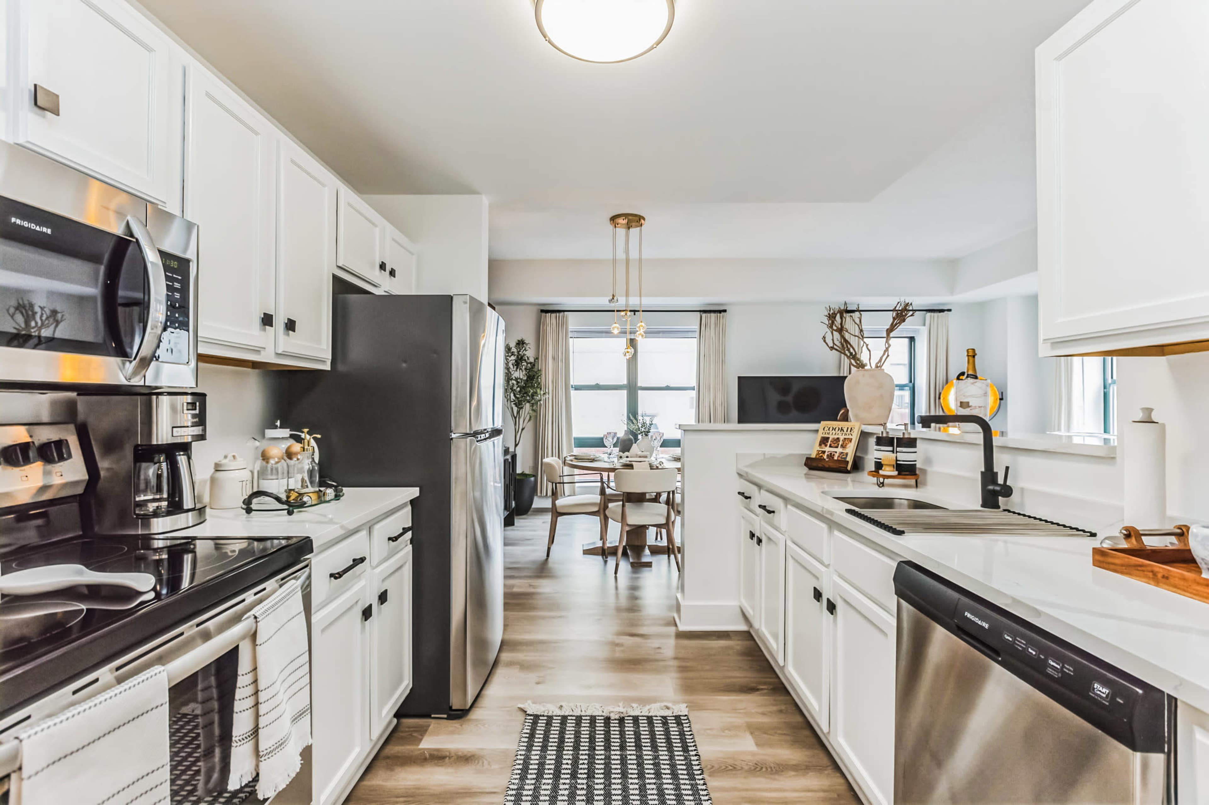 A modern kitchen with white cabinetry, stainless steel appliances, and a view leading into a dining area with a round table.