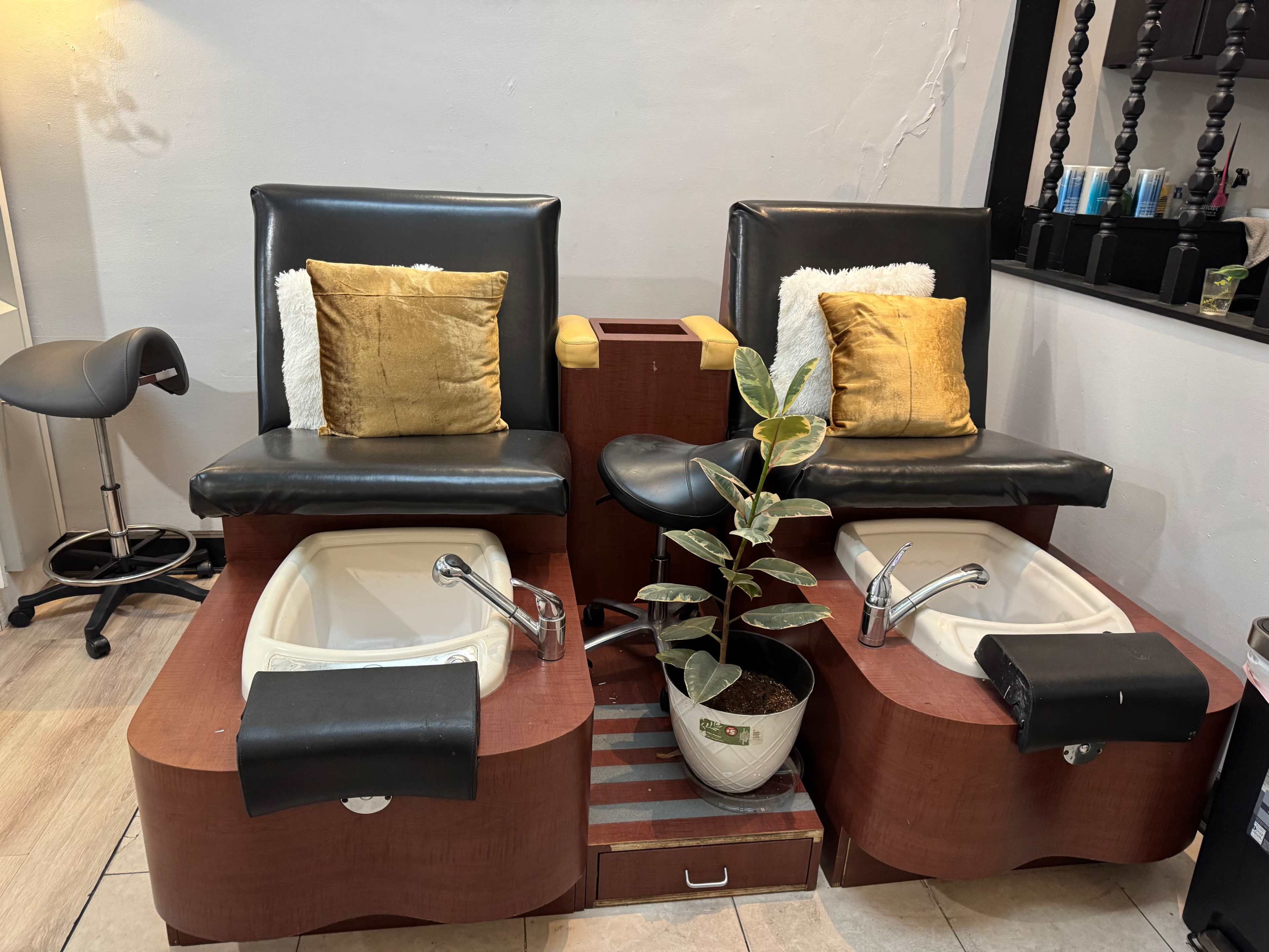 The image shows two pedicure chairs with black cushions, each equipped with a foot basin and a small potted plant between them.