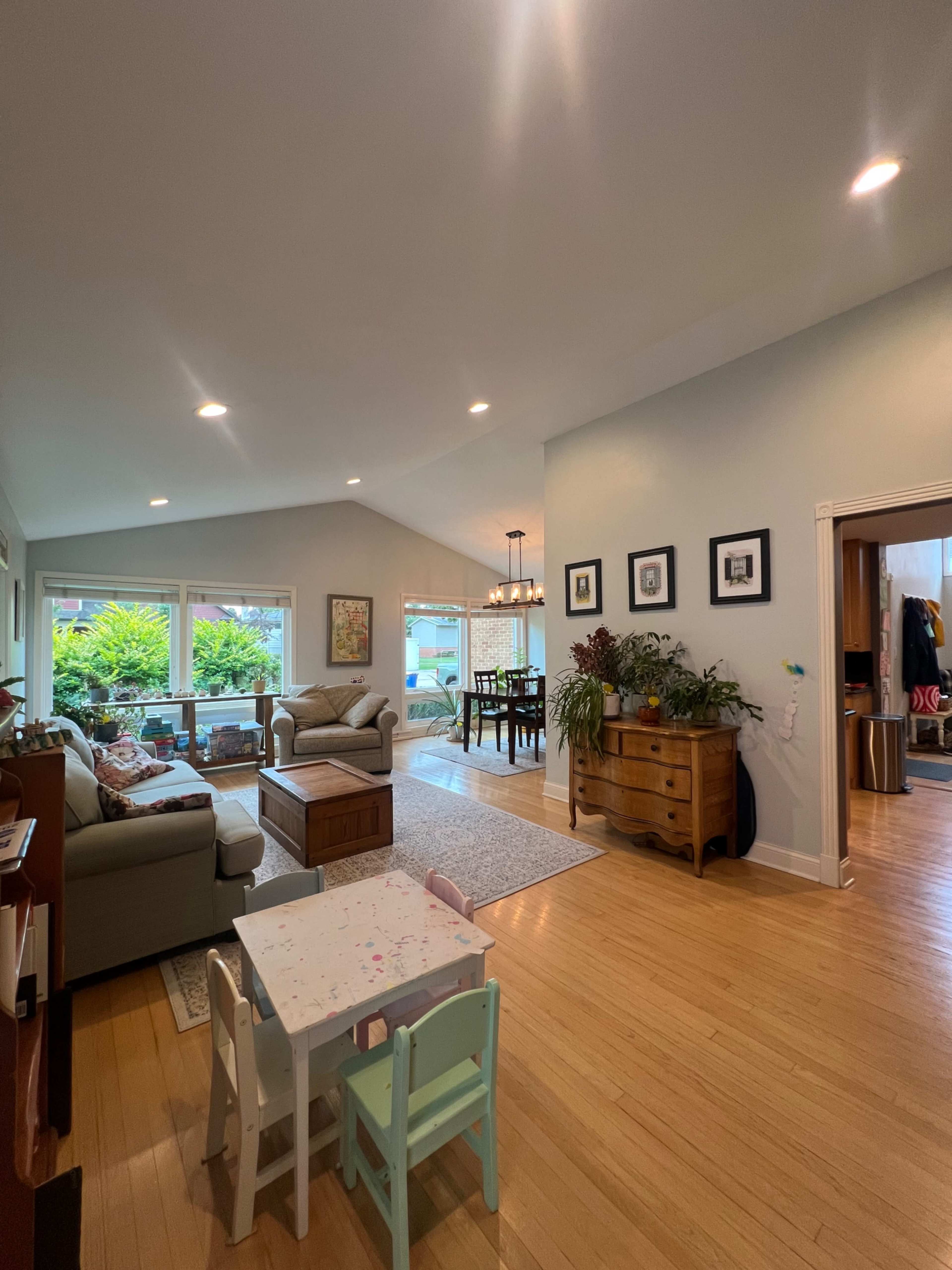 The image shows a spacious living area with a sofa, a dining table in the background, and a small children's table near a large window.