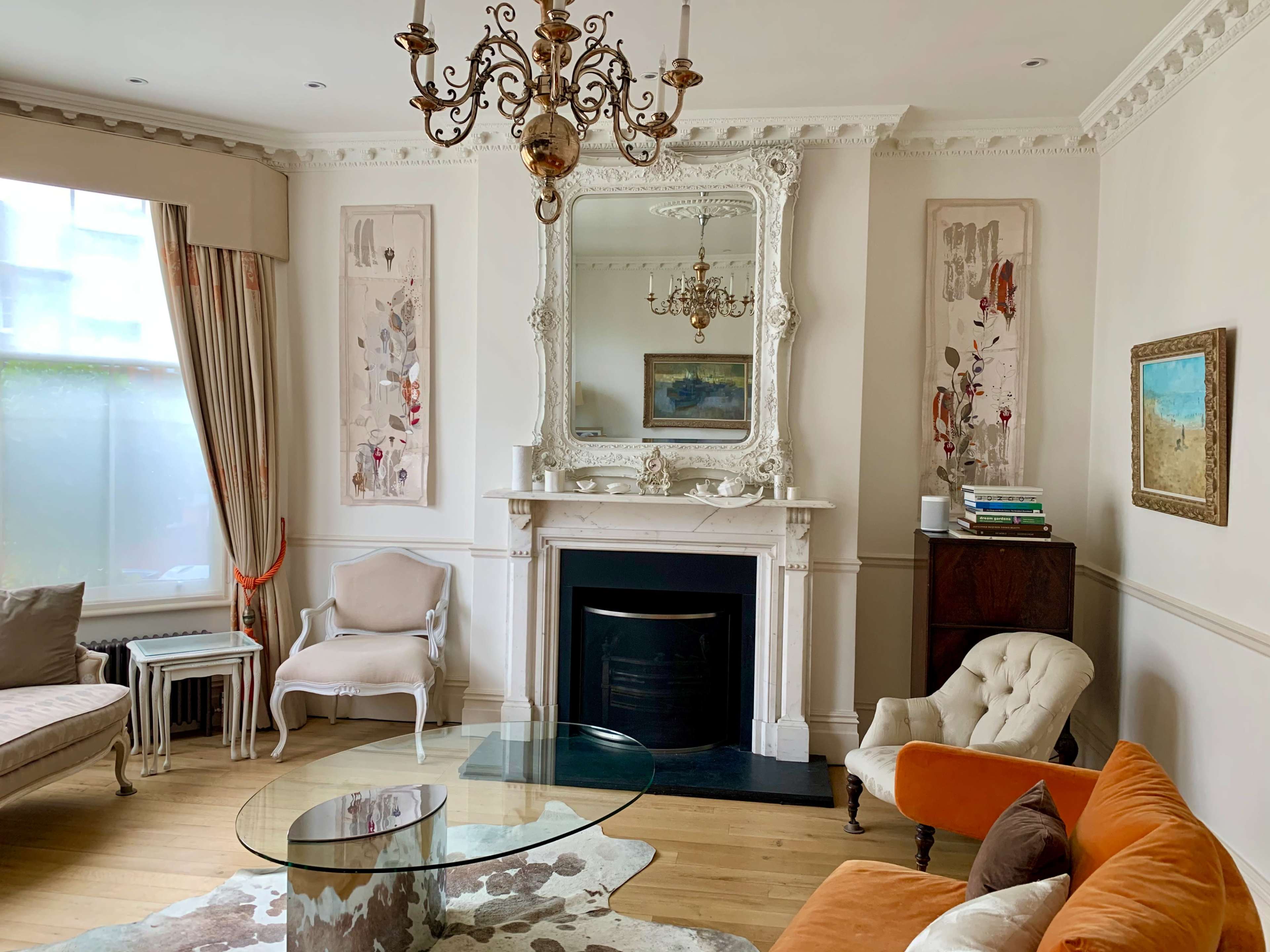 A living room featuring a mirror above a fireplace, a glass coffee table, an orange sofa, and decorative wall art.